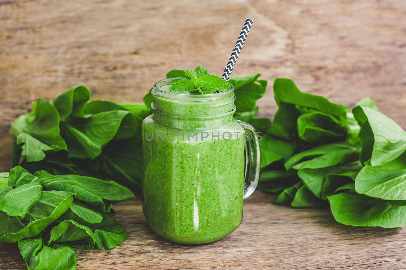 Mason jar mugs filled with green spinach, banana and coconut milk health smoothie with with a spoon of oatmeal on wooden rustic table by galitskaya