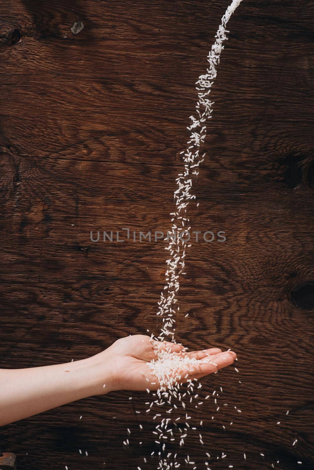 Dropping rice grain into hand isolated on wooden background by makidotvn