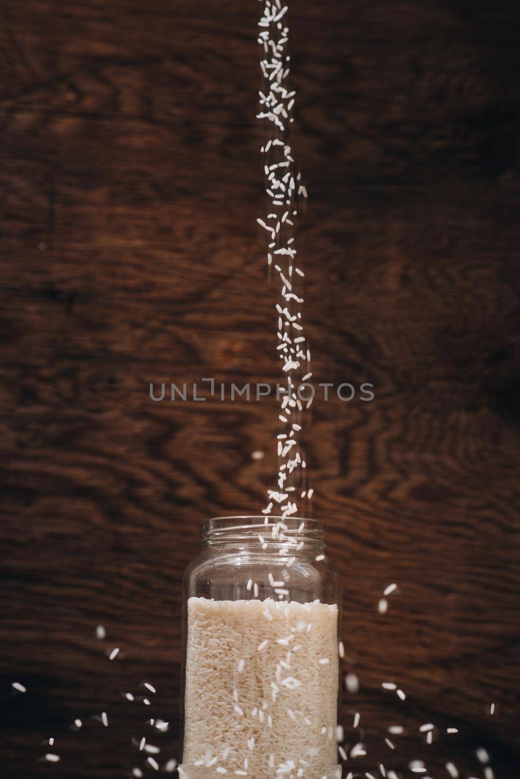 Rice grain pouring into jar on wooden background by makidotvn