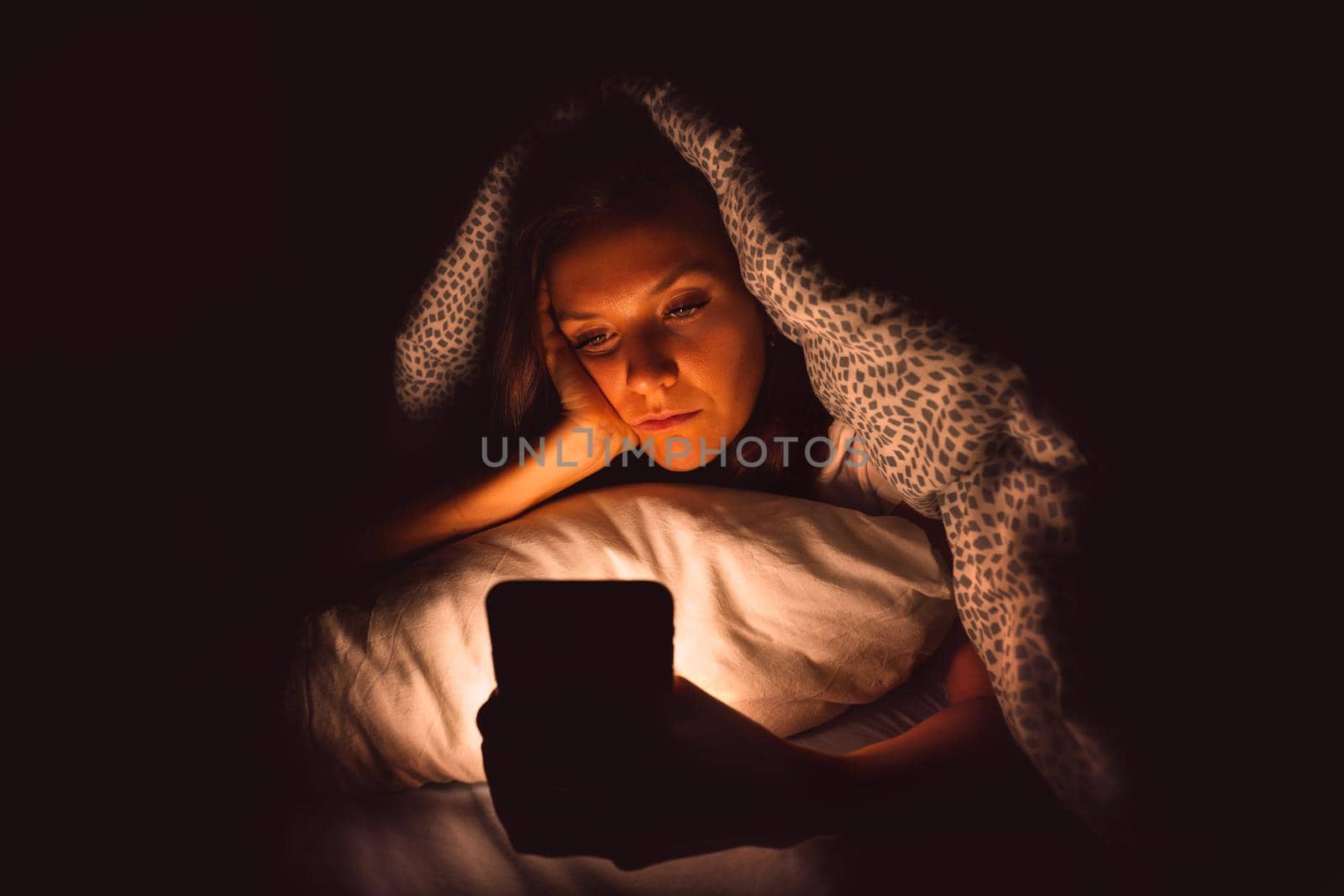 Young woman lying in bed and using smartphone at night before sleeping. Social media addiction and insomnia by DariaKulkova