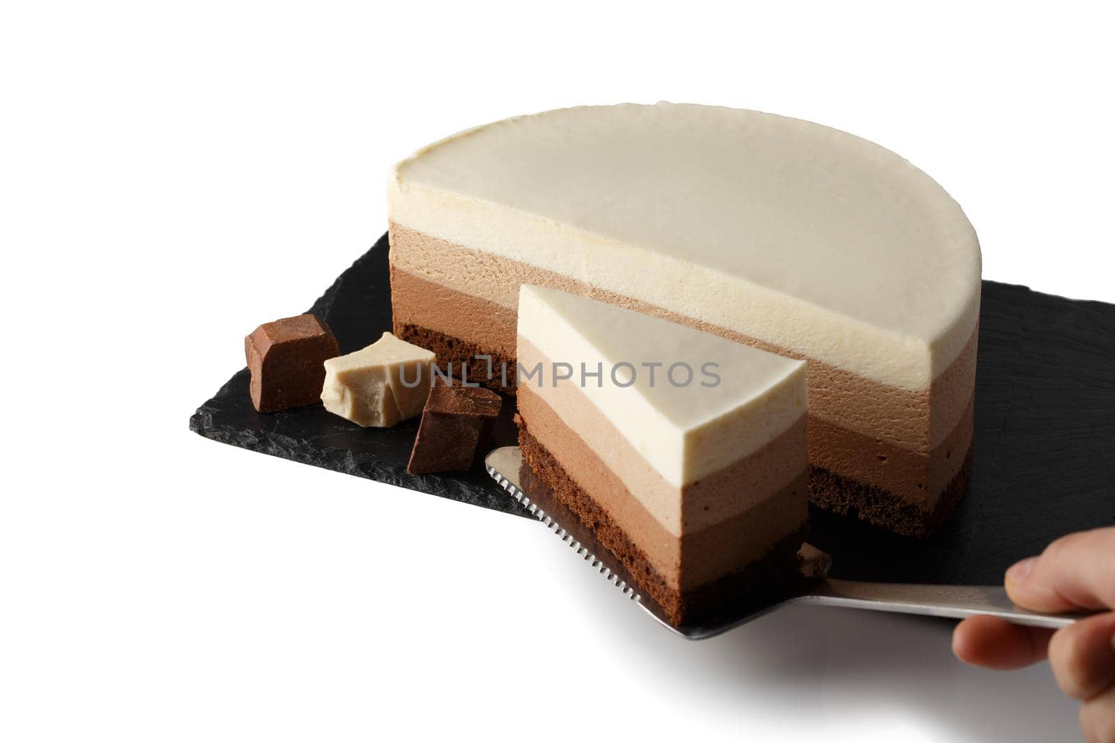 Delicious cake with three different kind of chocolate on plate of shale. Isolated on white background. Cook picks up a cut piece of cake on a pastry spatula.
