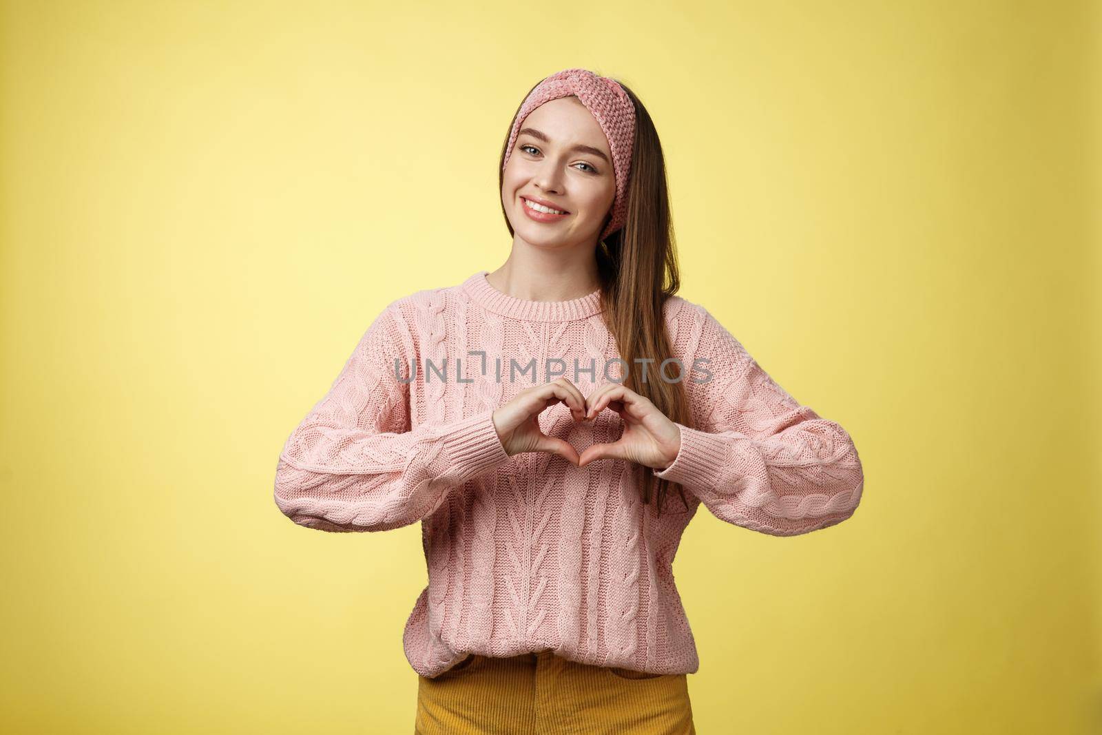 Girl brings peace and love, smiling tender, lovely showing heart gesture over chest, adoring, liking making romantic gestures feeling sympathy, passion and romance in air, posing in sweater.