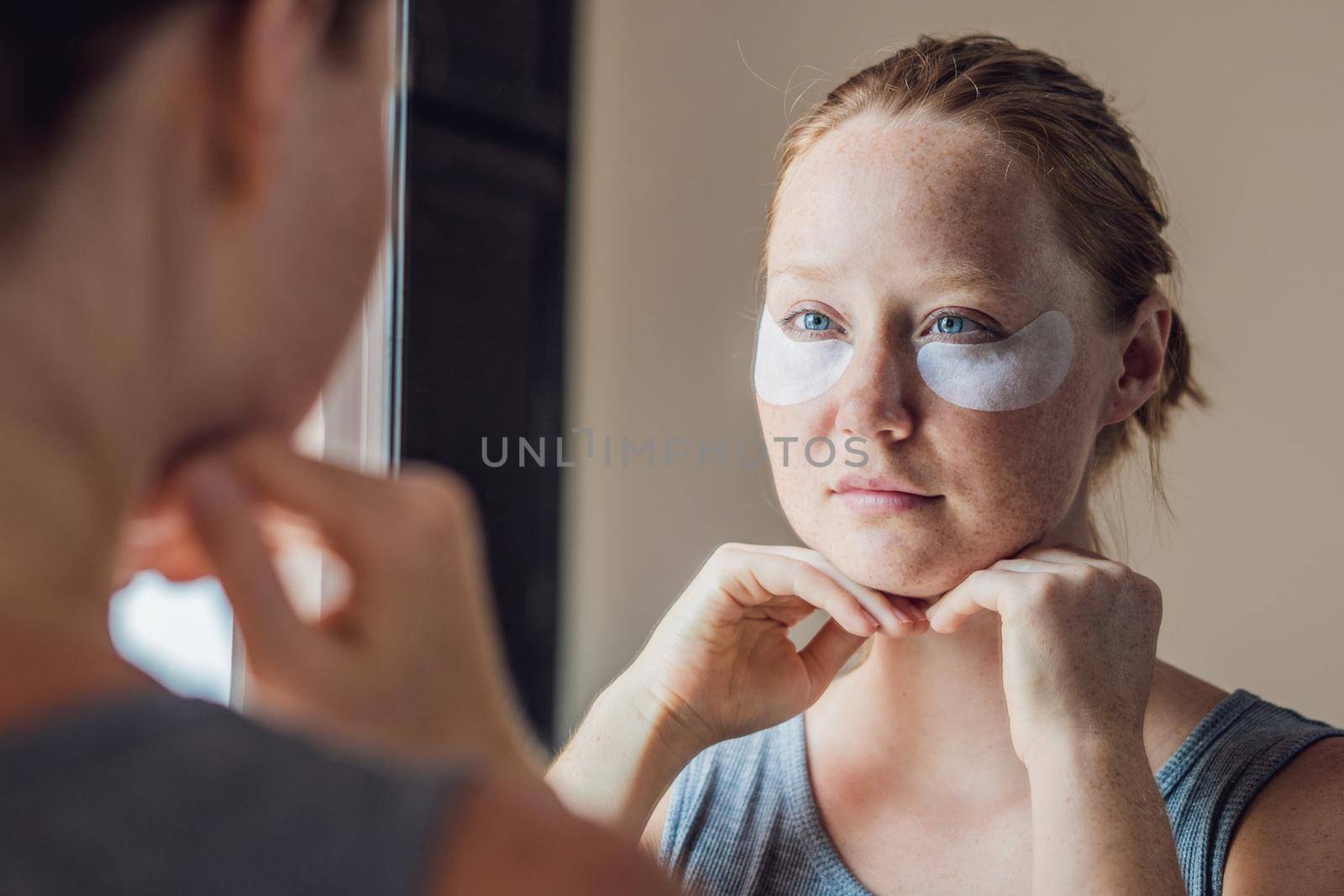 Portrait of Beauty Red-haired woman with eye patches showing an effect of perfect skin. Spa Girl.