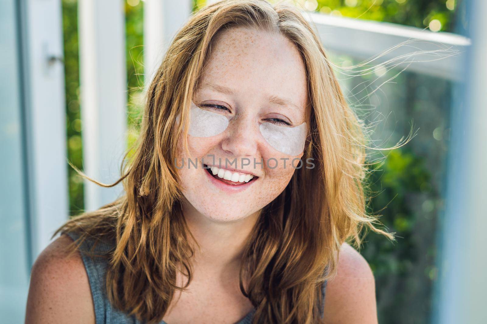 Portrait of Beauty Red-haired woman with eye patches showing an effect of perfect skin. Spa Girl.