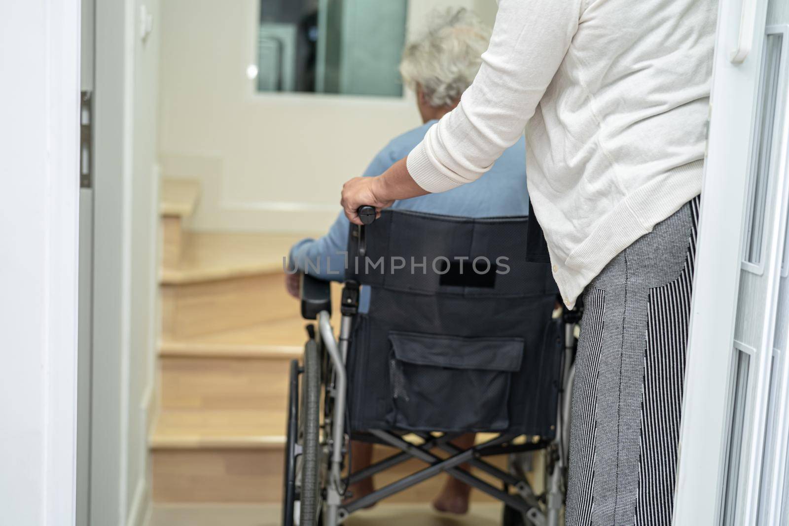 Caregiver help asian or elderly old woman sitting wheelchair support up the stairs in home. by pamai