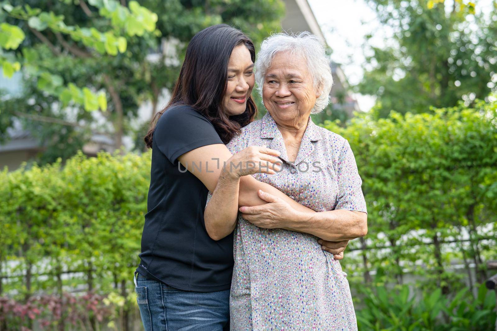 Asian elderly woman with caregiver daugther walking and hug with happy in nature park.