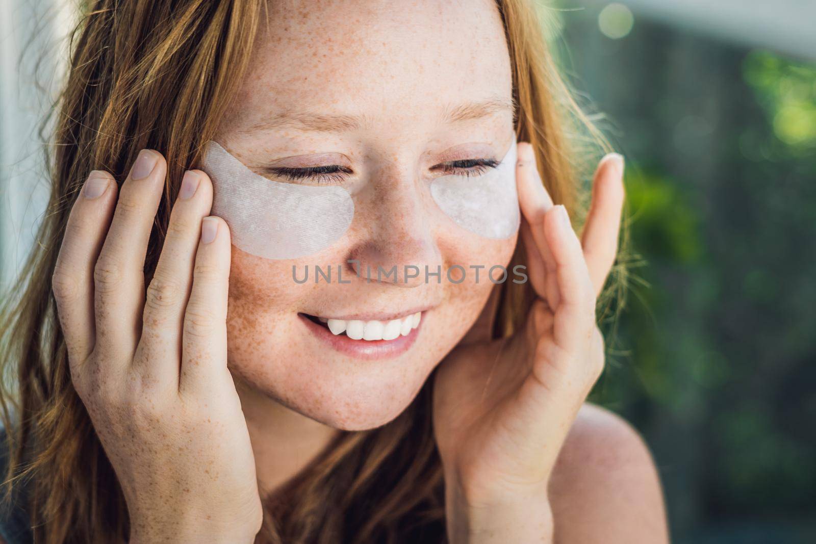 Portrait of Beauty Red-haired woman with eye patches showing an effect of perfect skin. Spa Girl.