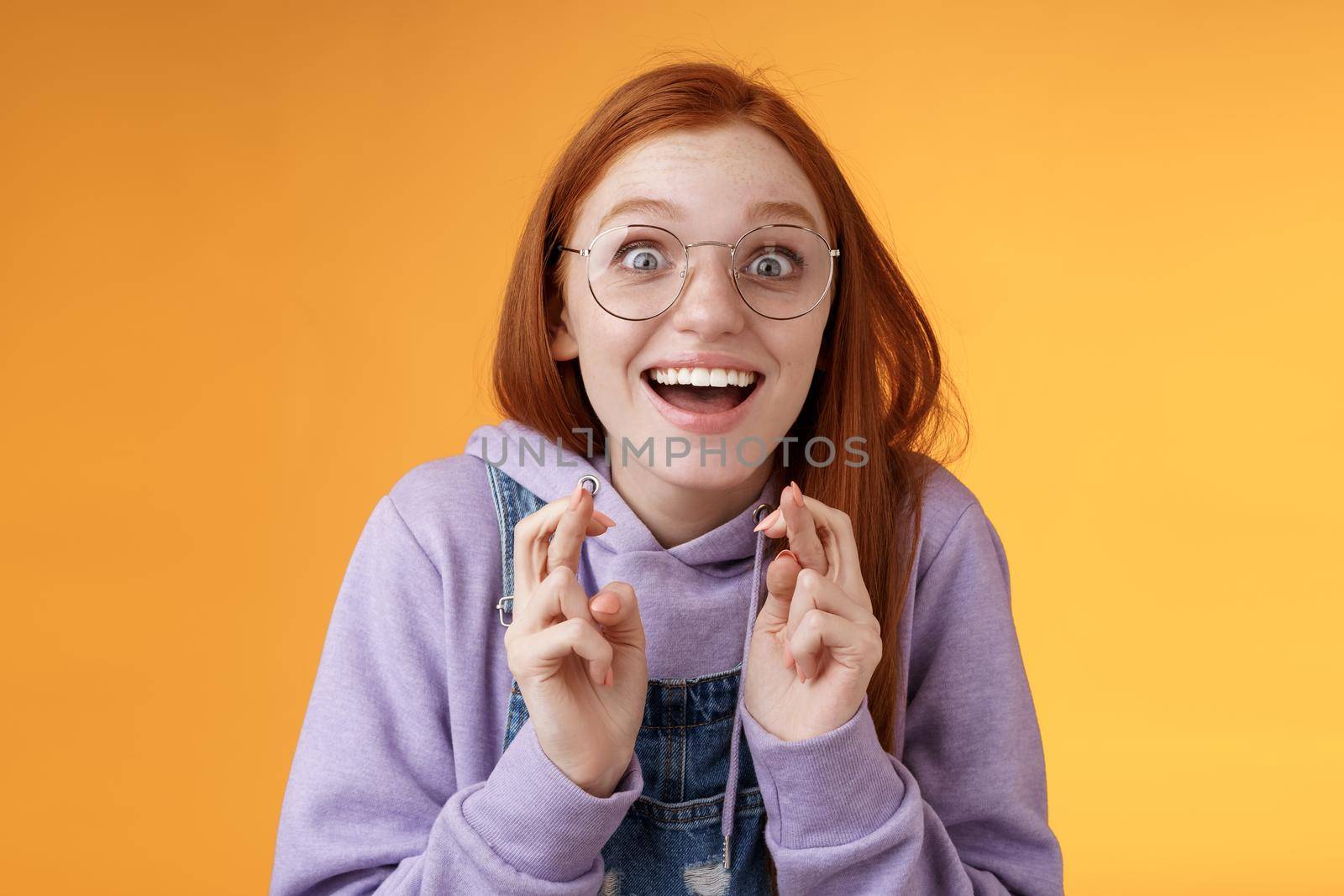 Surprised girl dream came true celebrating standing amused excited cross fingers good luck wish fulfilled smiling emotive thrilled finally win receive good news optimistic hopeful orange background by Benzoix