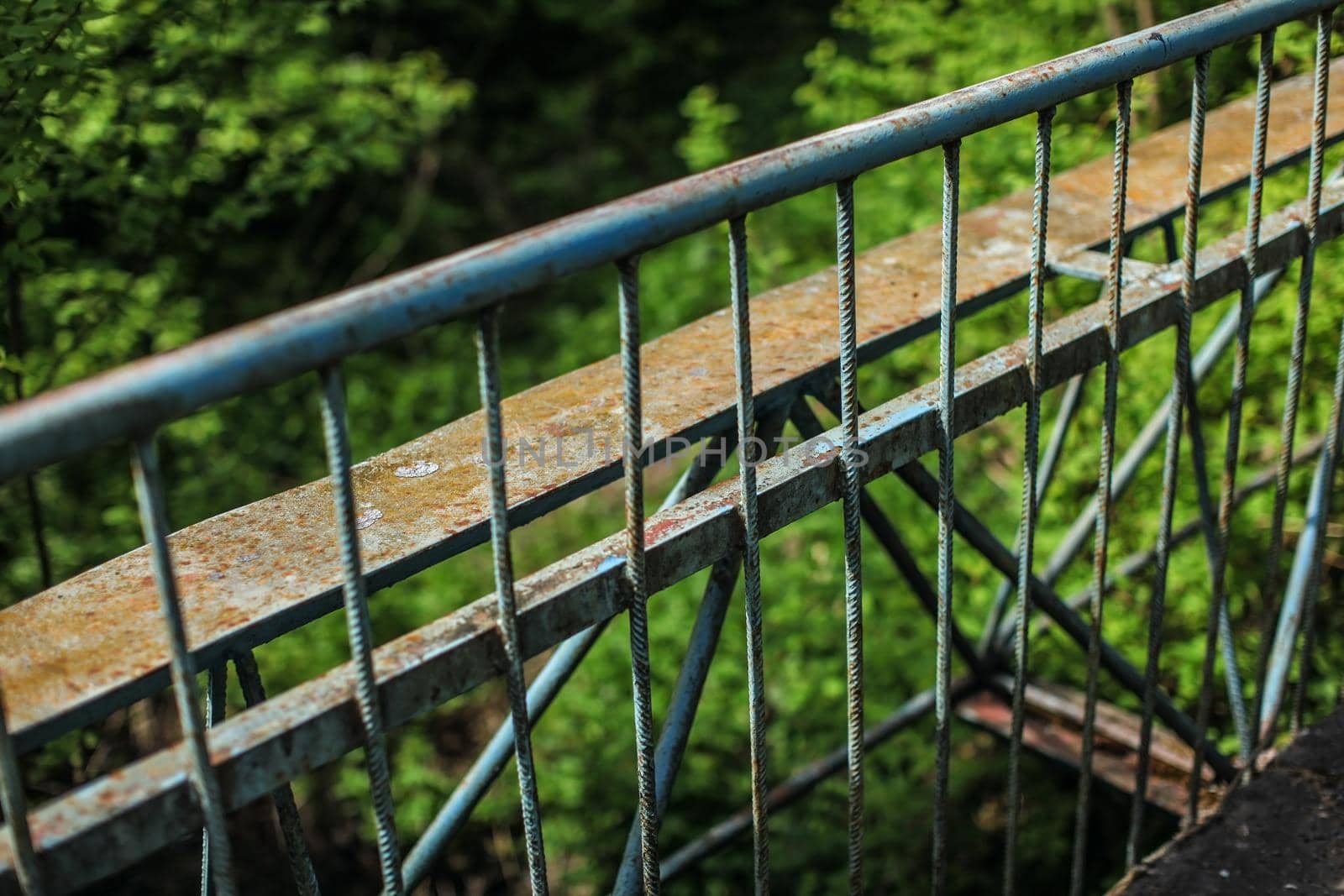 Old metal guard rail of bridge, with blurred green forest in background.