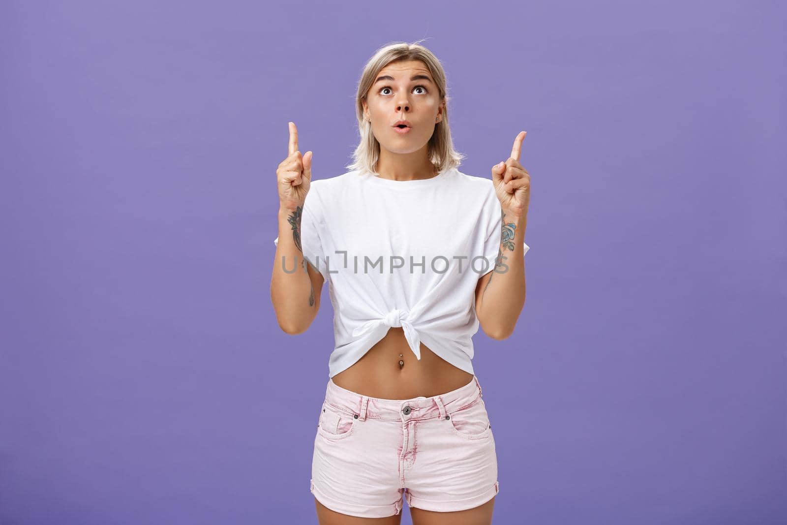 Girl dreaming become flight attendant being amazed with cool airplane flying in sky looking up with surprised impressed look saying wow pointing upwards posing over purple background. Copy space