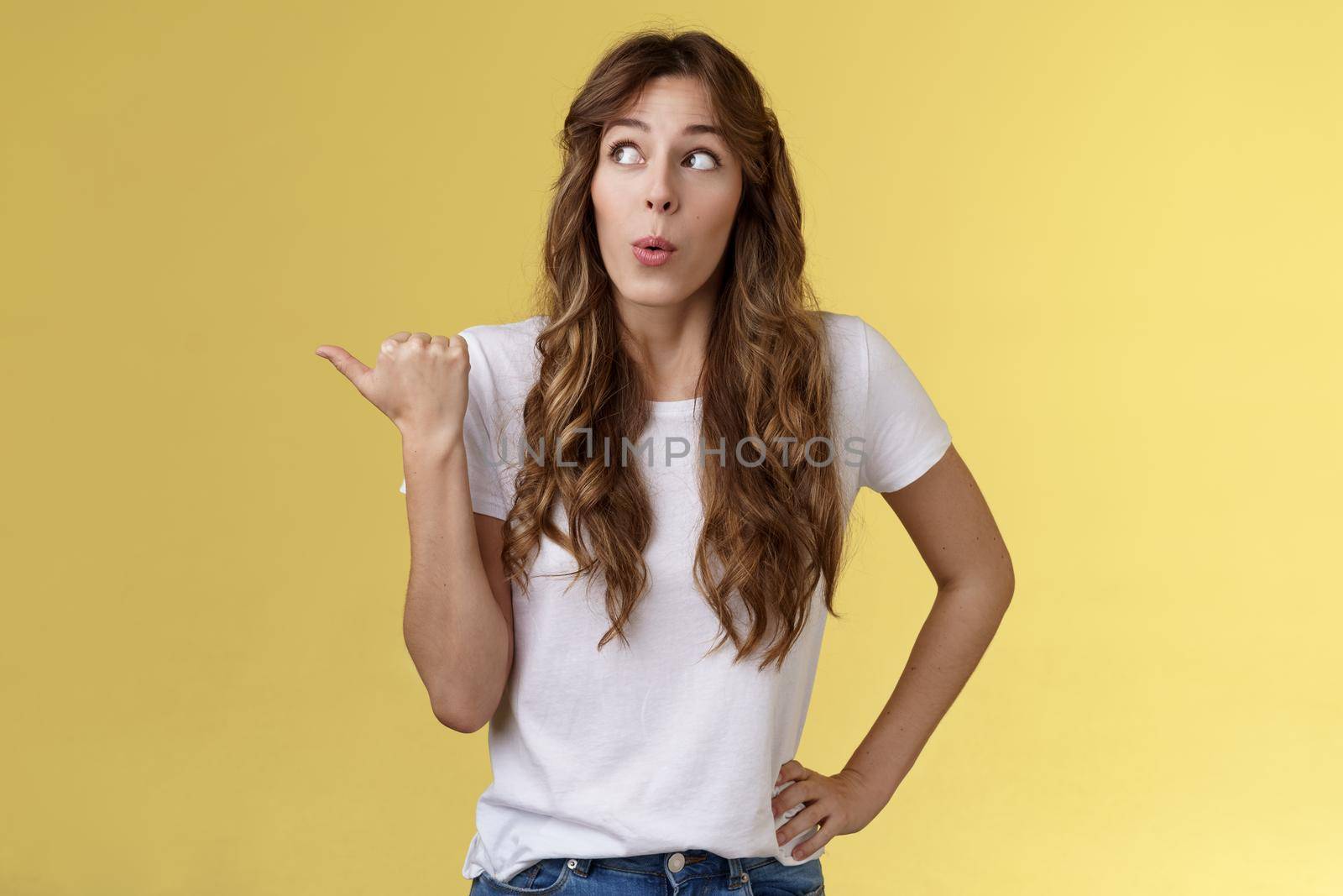 Girls gossiping discuss funny neighbours. Curious outgoing cute funny curly-haired woman look pointing thumb left fold lips wow amused glancing intrigued learn juicy rumor stand yellow background by Benzoix