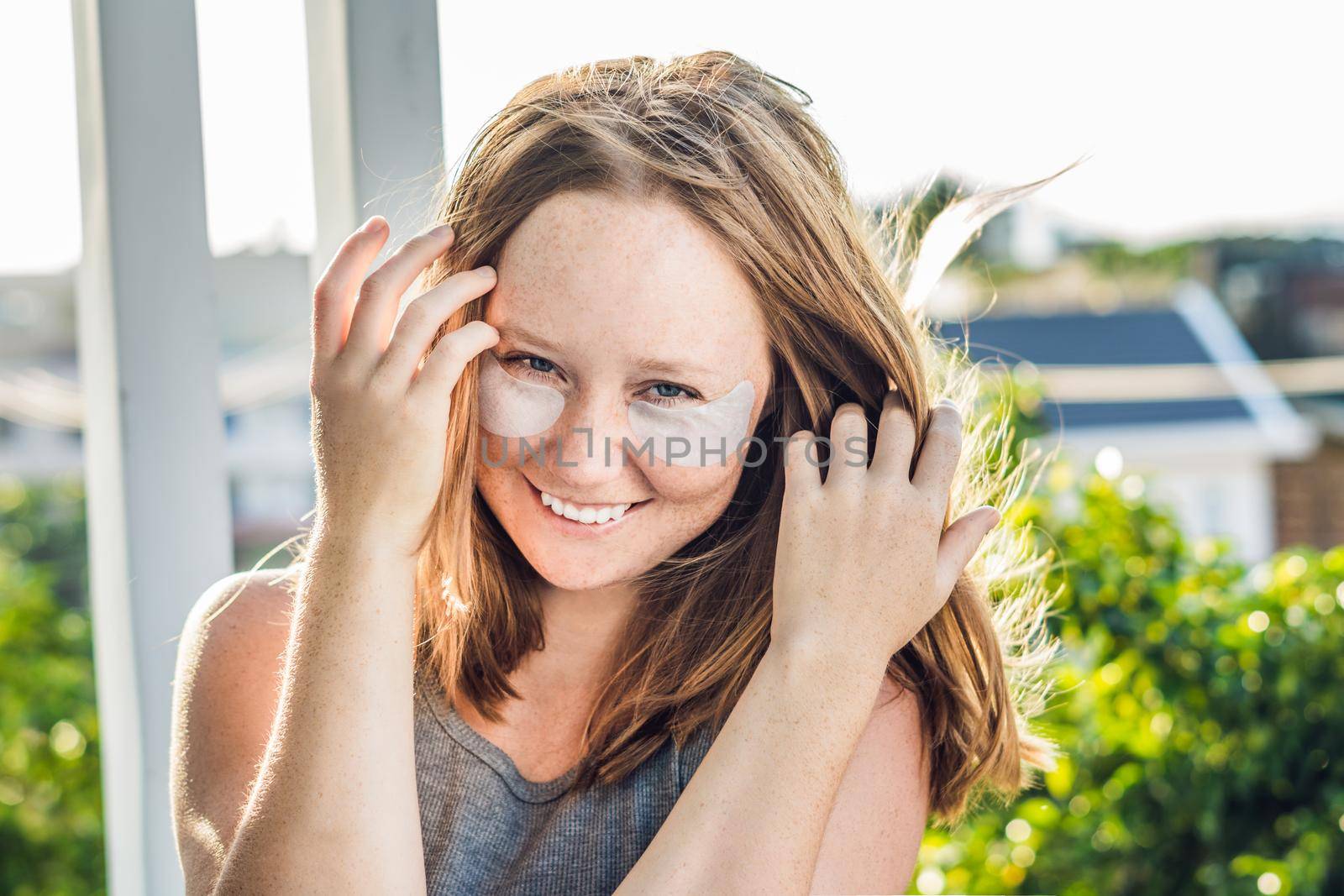 Portrait of Beauty Red-haired woman with eye patches showing an effect of perfect skin. Spa Girl.