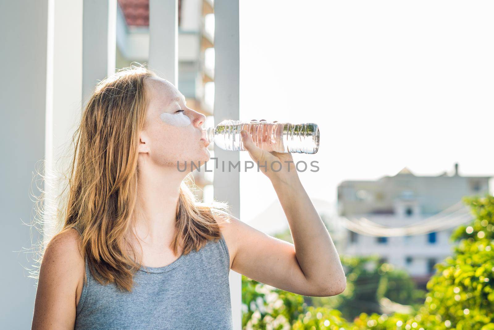 Portrait of Beauty Red-haired woman with eye patches drinks water. Spa Girl.