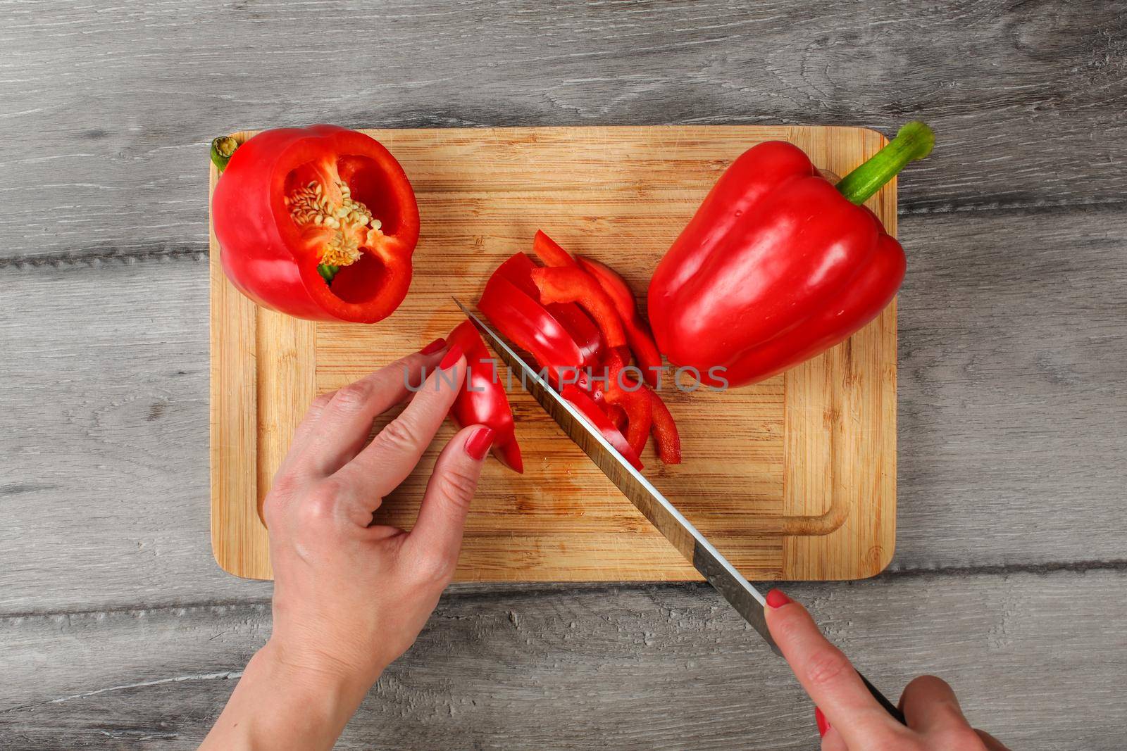 Table top view, woman hands holding chef knife cutting red bell pepper on old chopping board.