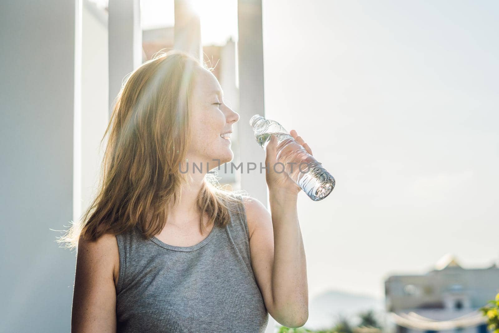 Young woman is drinking water on the sunset background.