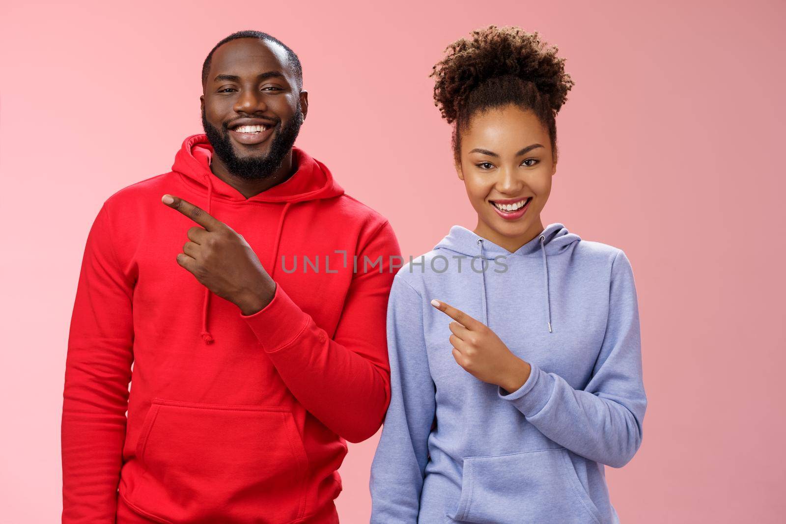 Charming carefree smiling african american two man woman grinning white teeth having fun fool around together pointing upper left corner showing couple project proudly, standing pink background.