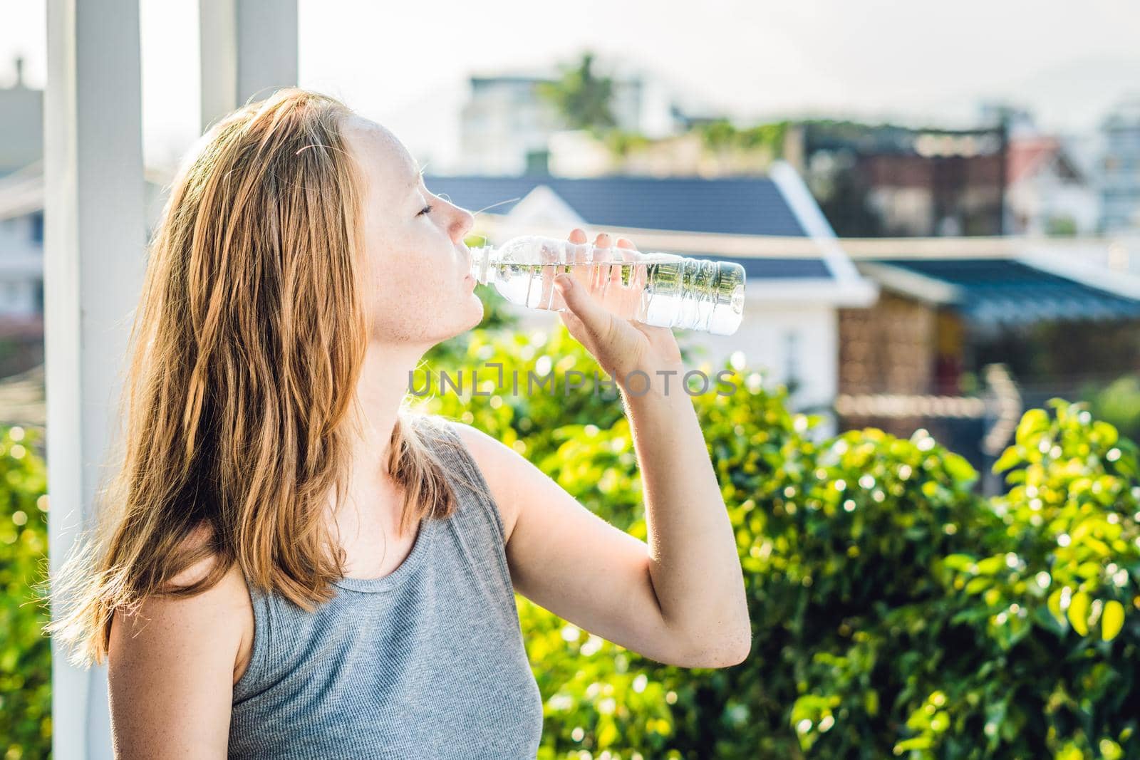 Young woman is drinking water on the sunset background.