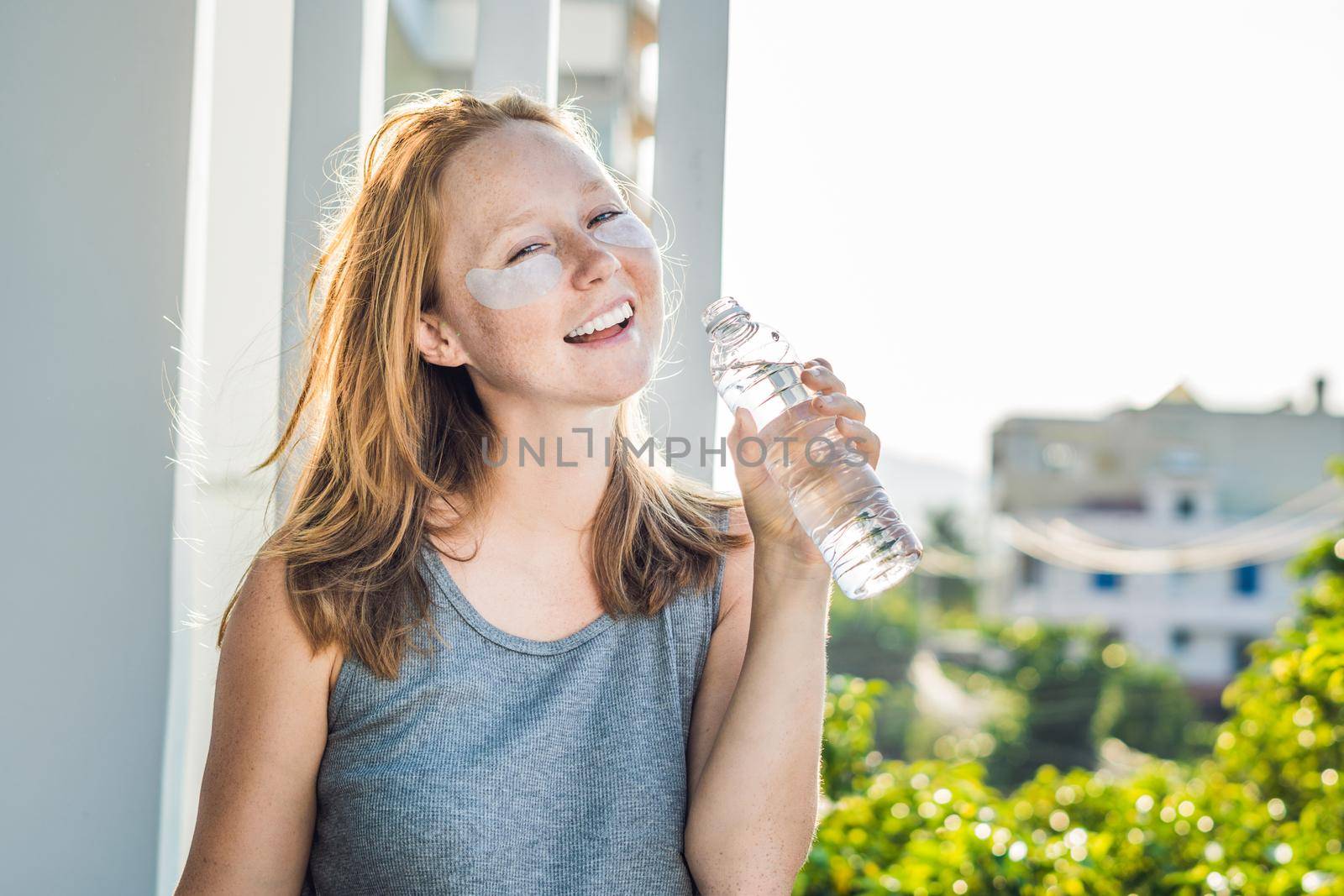 Portrait of Beauty Red-haired woman with eye patches drinks water. Spa Girl.