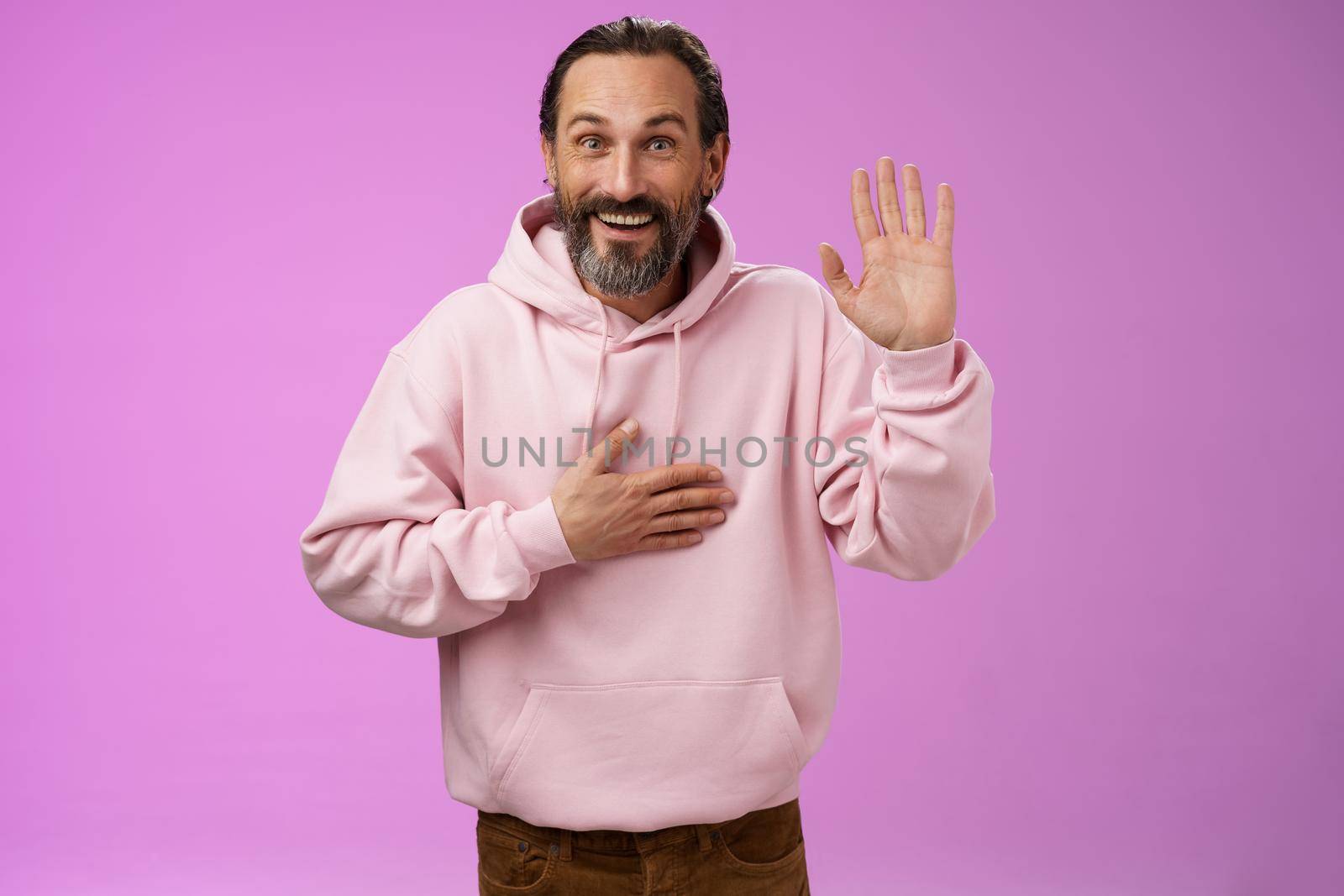 Charismatic sincere optimistic lucky european mature 40s man bearded pleding swearing tell truth hold hand heart raise palm make promise joyfully, standing purple background smiling white teeth.