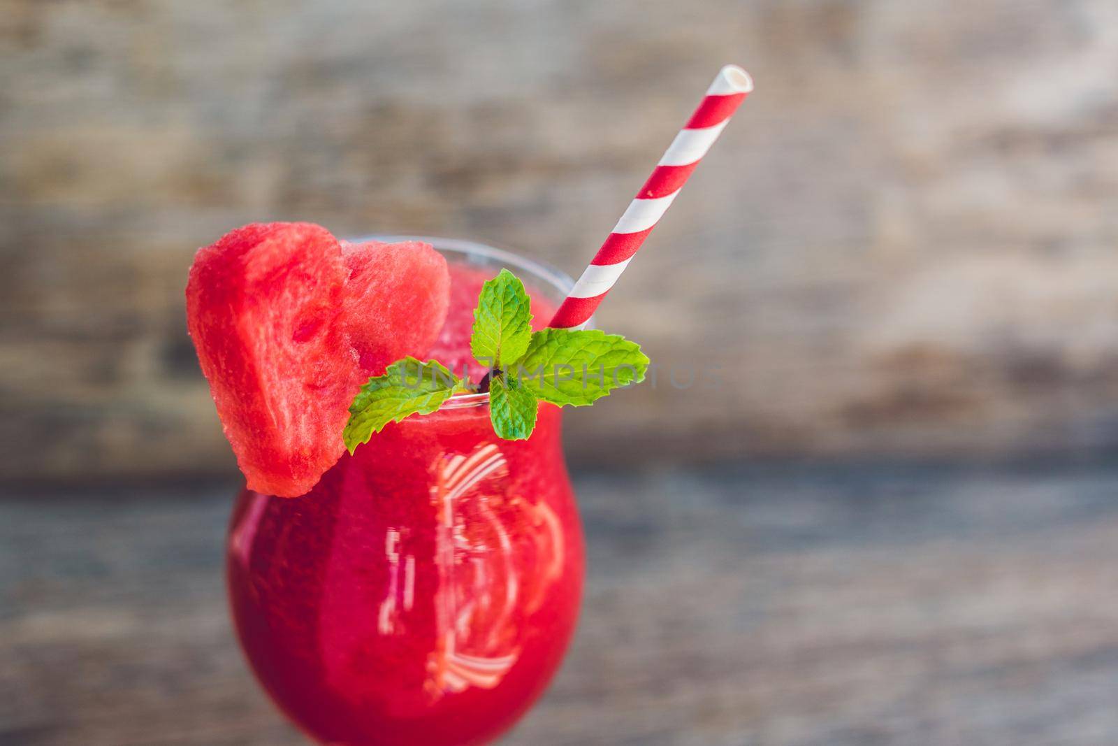 Healthy watermelon smoothie with mint and striped straws on a wood background.