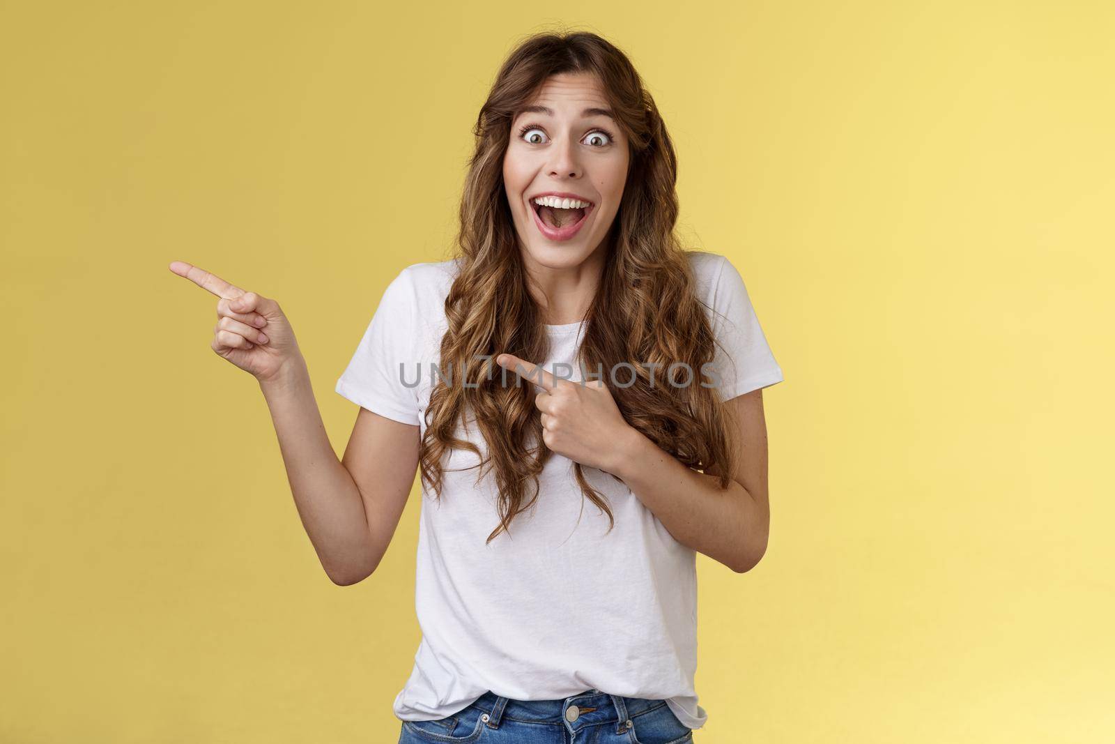 Happy sincere cheerful young surprised woman see celebrity lose speech stare excited unbelievable awesome luck fascinated pointing index fingers left open mouth stunned thrilled yellow background by Benzoix