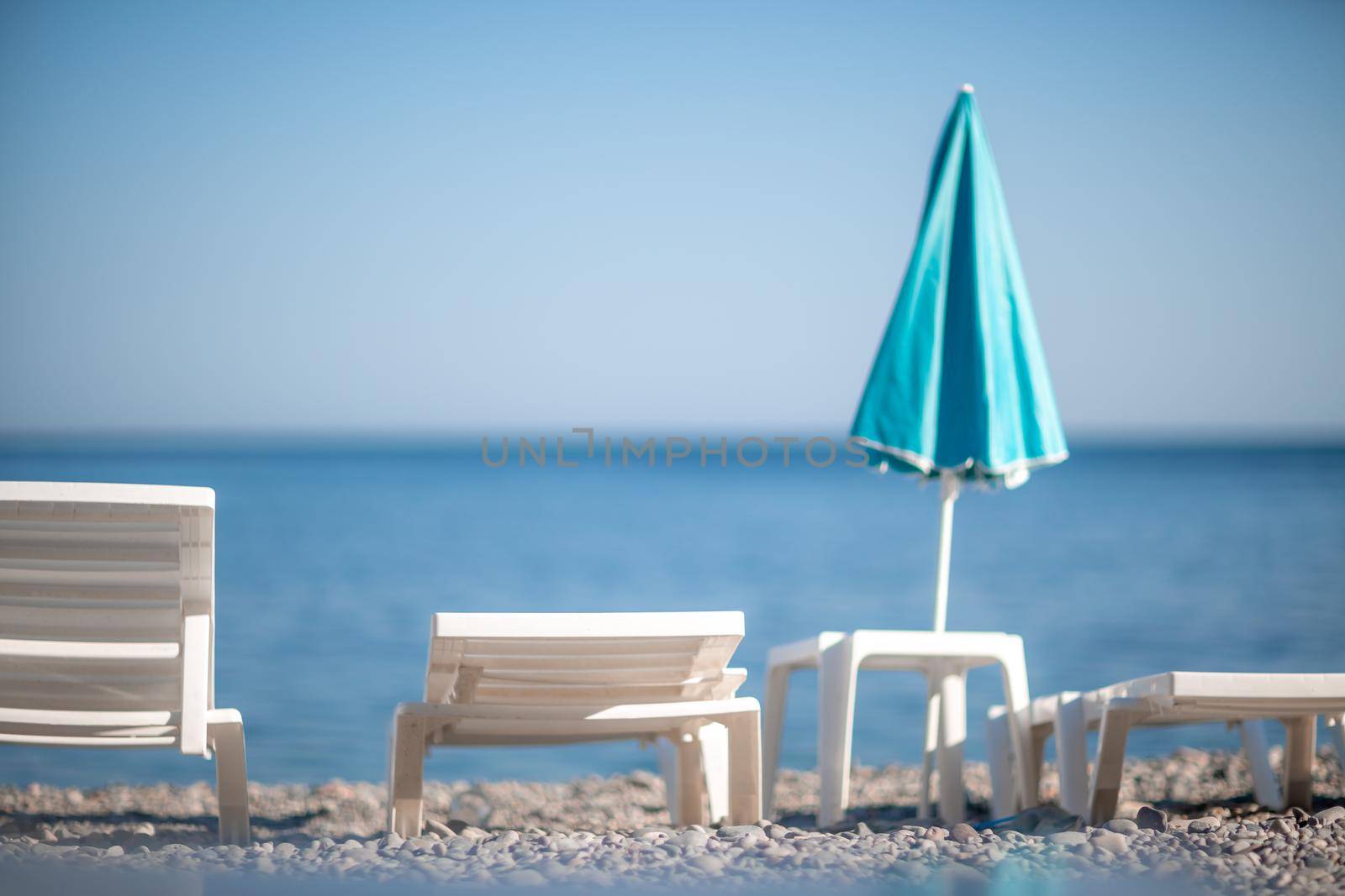 Several white sun loungers and a turquoise parasol on a deserted beach. The perfect vacation concept