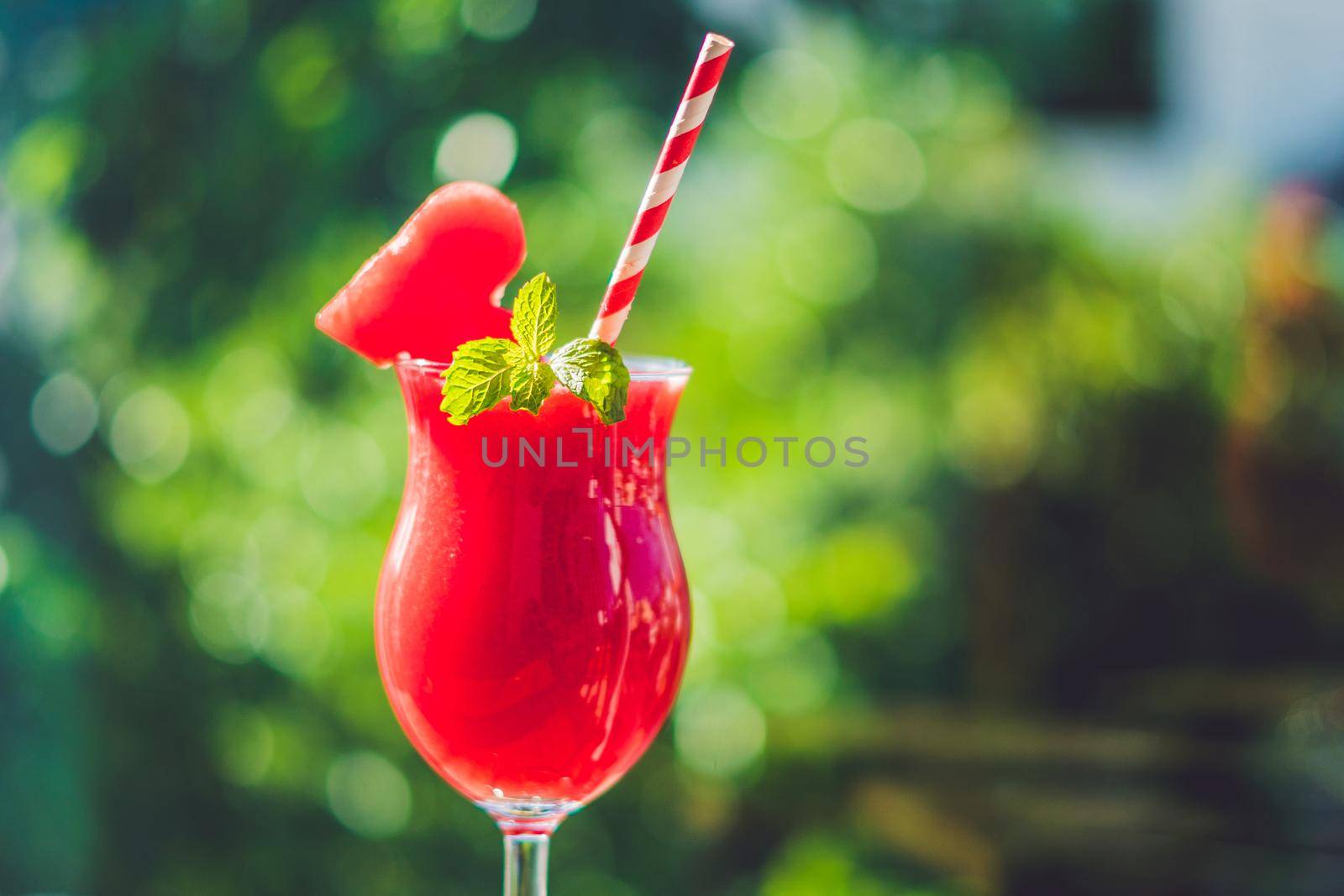 Healthy watermelon smoothie with mint and striped straws against the background of greenery.