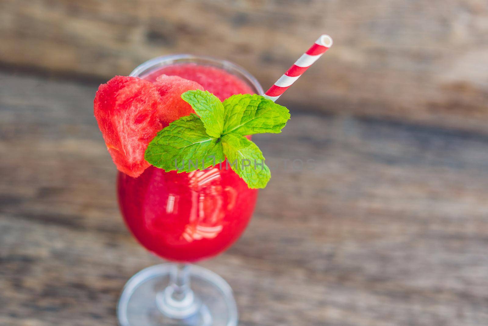 Healthy watermelon smoothie with mint and striped straws on a wood background.