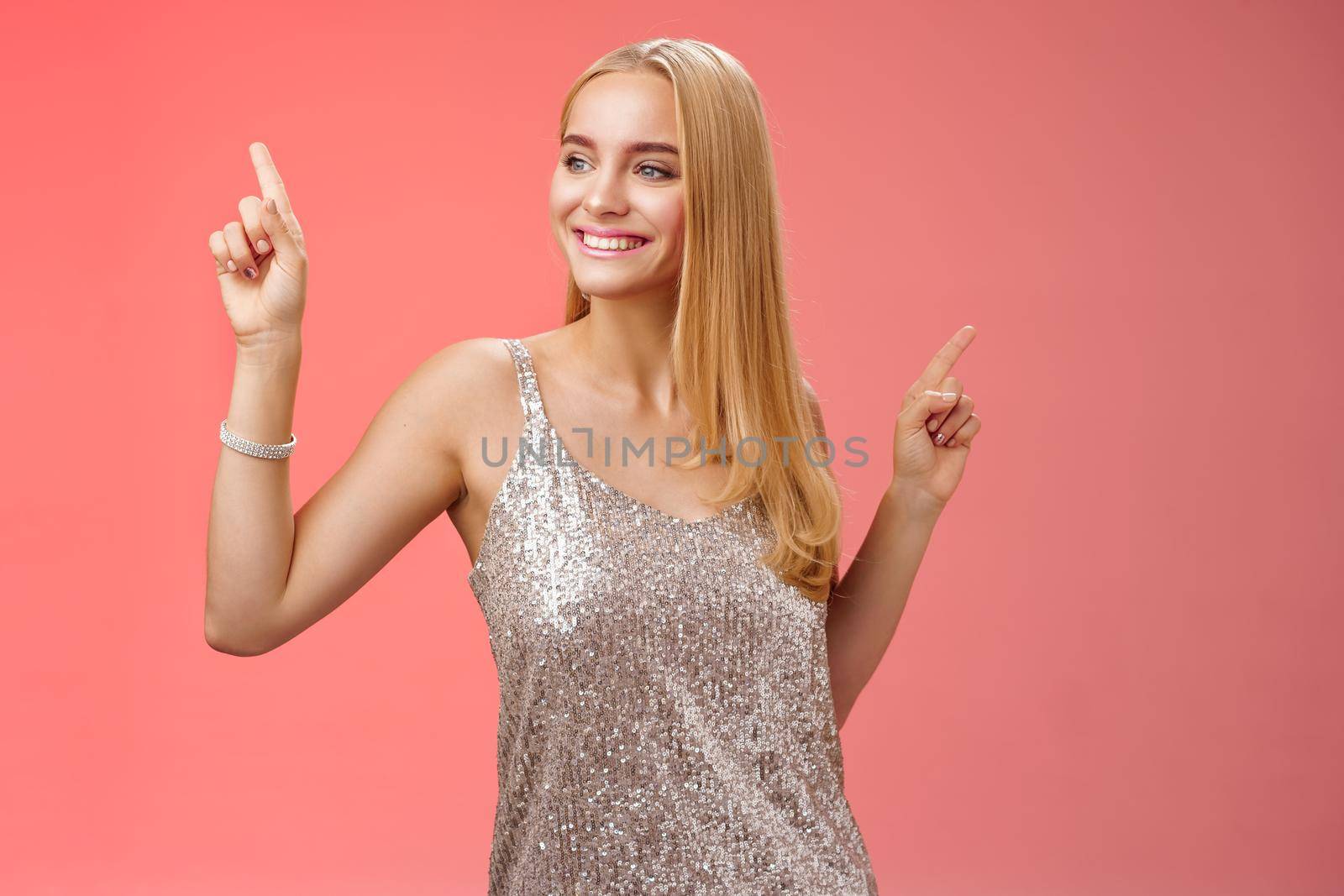 Carefree good-looking stylish glamour blond young 20s woman in silver glittering dress dancing having fun amused go wild party night prom shaking body raising index fingers up, red background by Benzoix