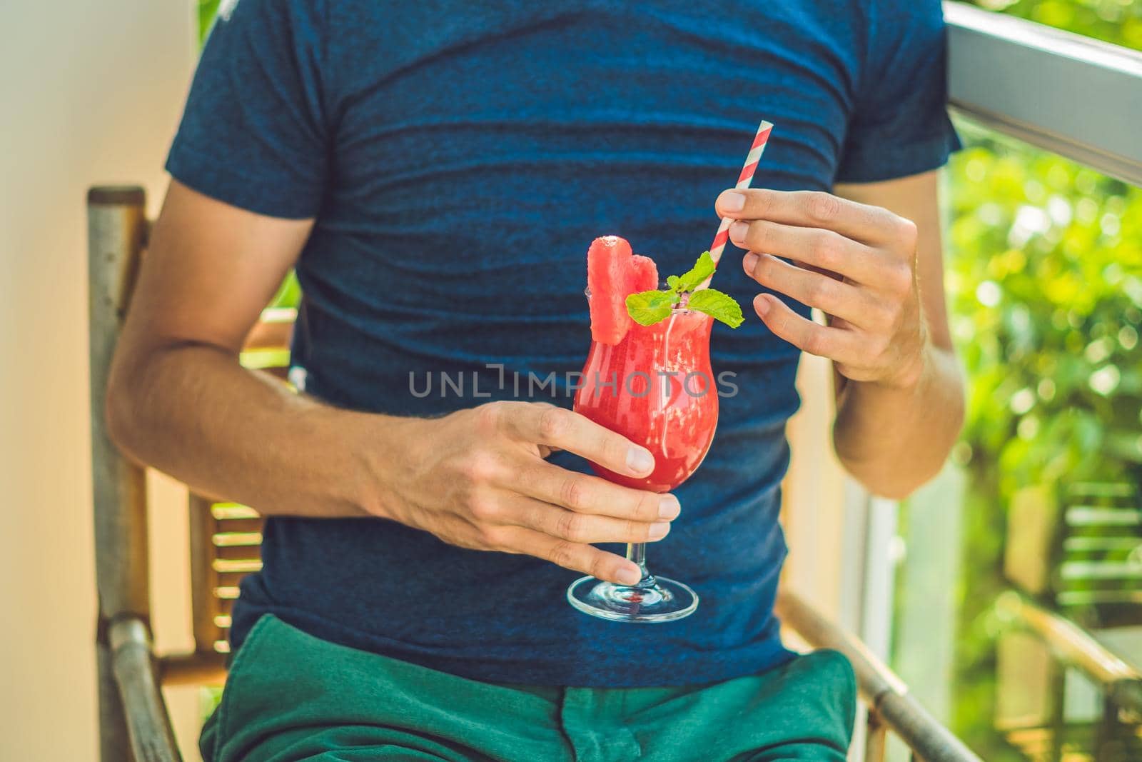 Man is holding Healthy watermelon smoothie with mint and striped straws on a wood background by galitskaya
