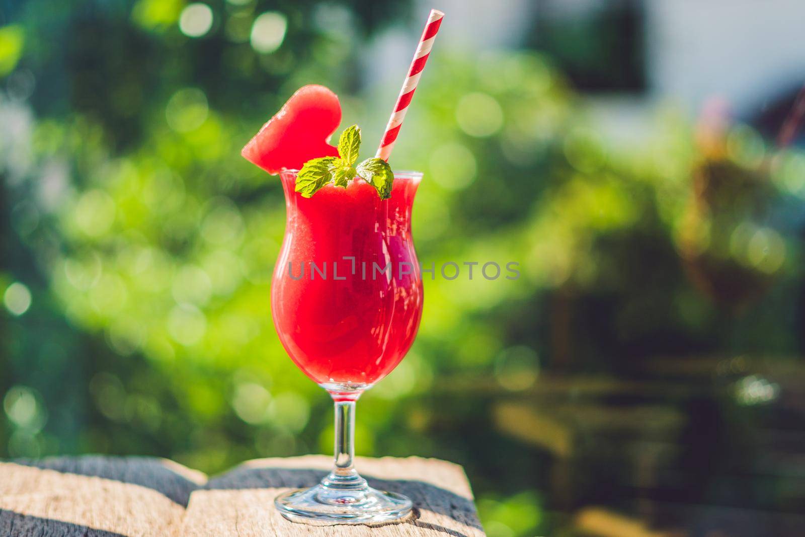 Healthy watermelon smoothie with mint and striped straws against the background of greenery.