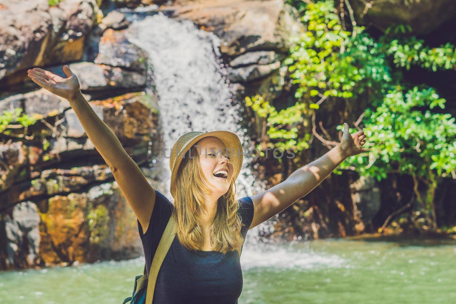 Young woman standing in front of waterfall with her hands raised. Female tourist with her arms outstretched by galitskaya