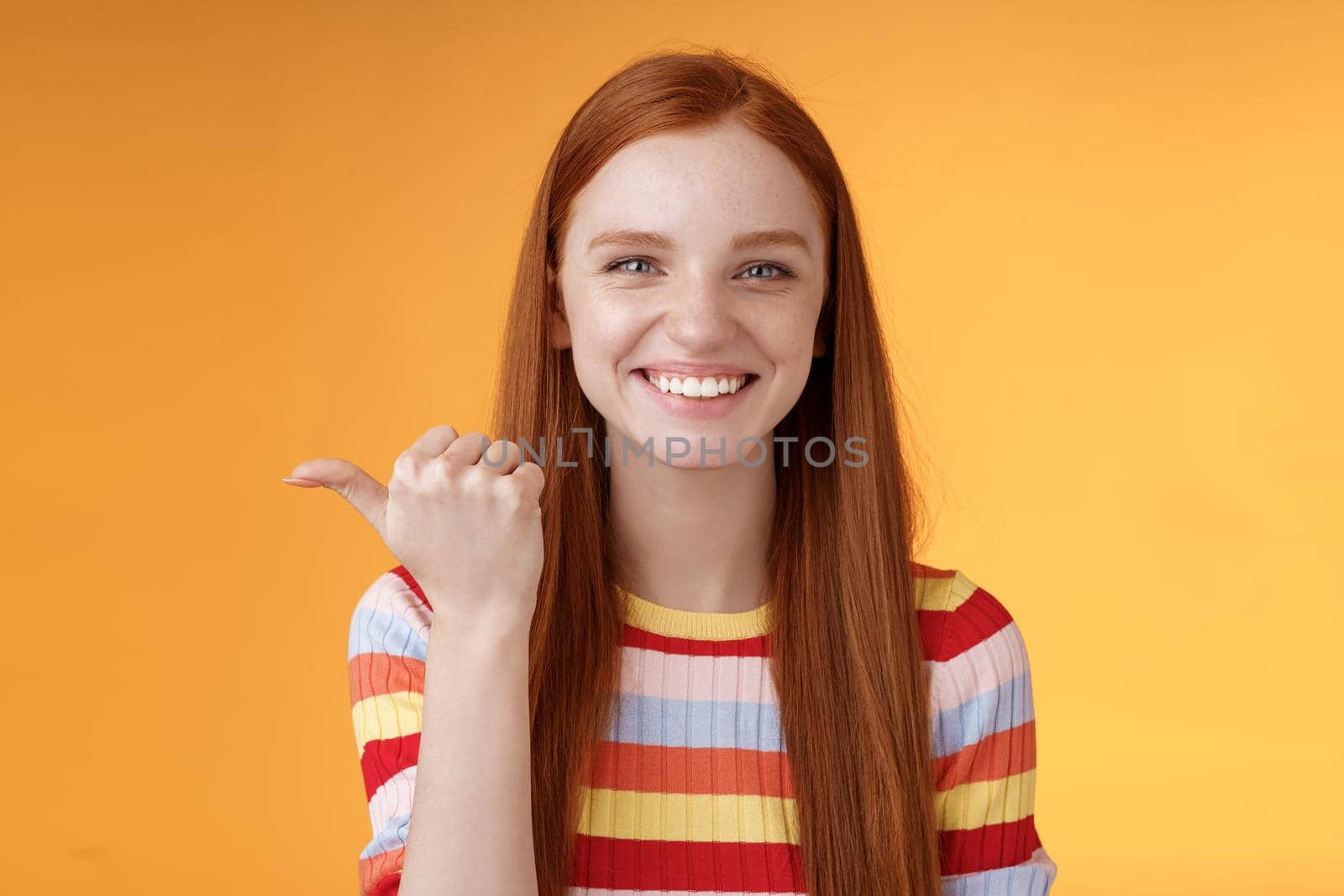 Girl pointing left cool person can help smiling delighted look friendly camera discuss interesting project introduce friend during conversation standing happy grinning orange background.