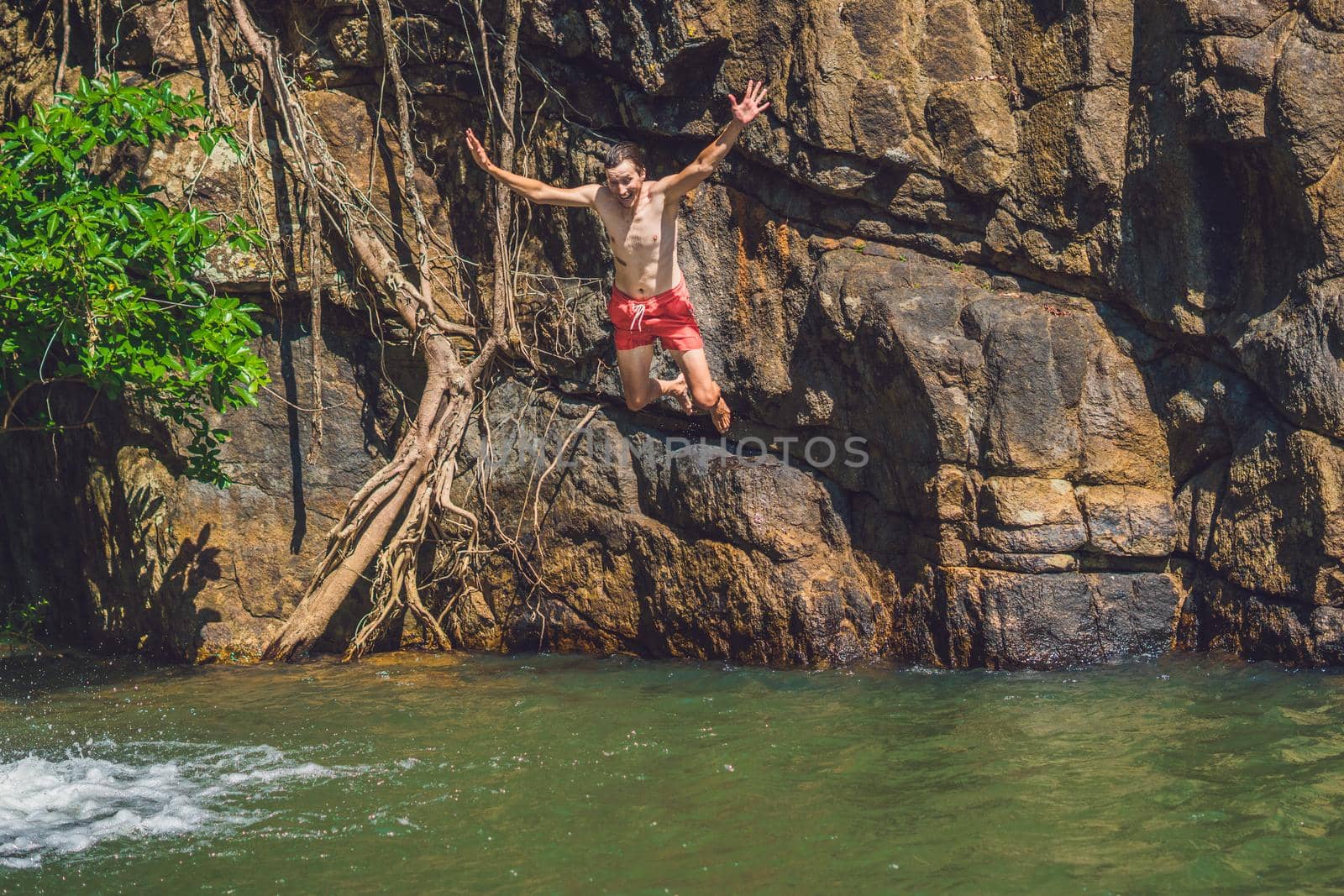 Man jumping off cliff into the water. Summer fun lifestyle.