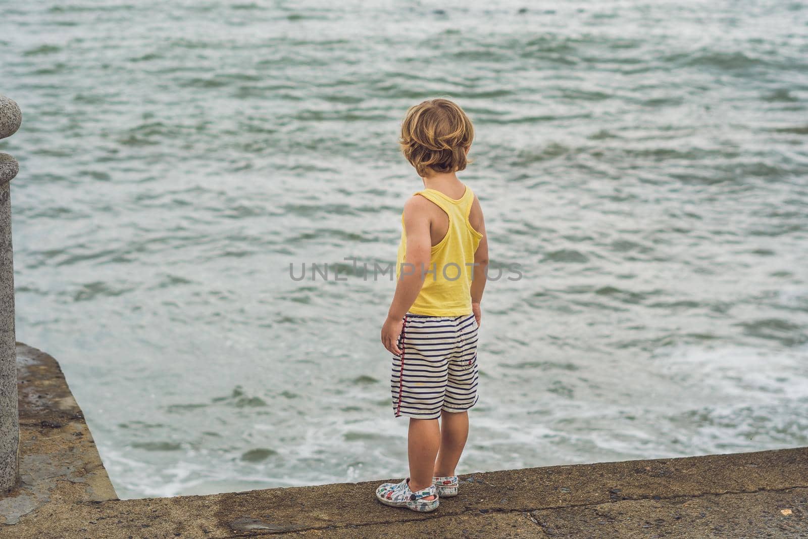 Cute boy stands on the shore watching the ocean waves.