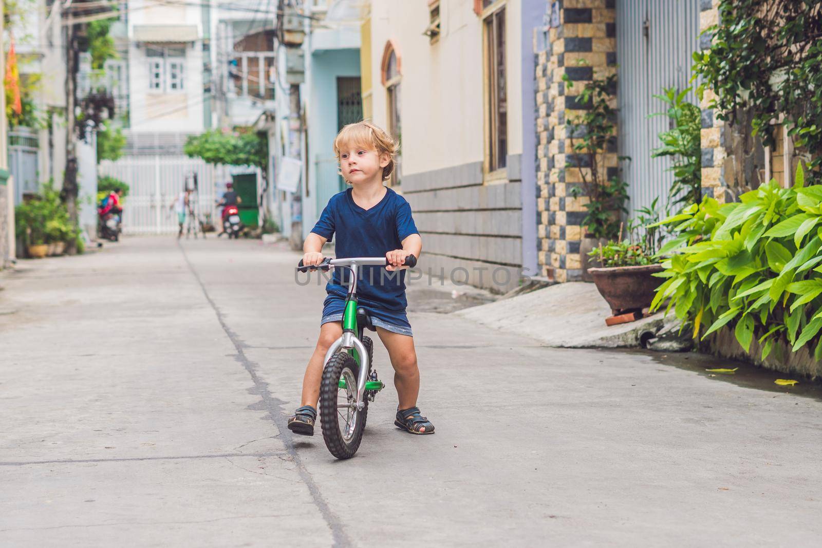 Active blond kid boy driving bicycle n the street of the city. Toddler child dreaming and having fun on warm summer day. outdoors games for children. Balance bike concept by galitskaya