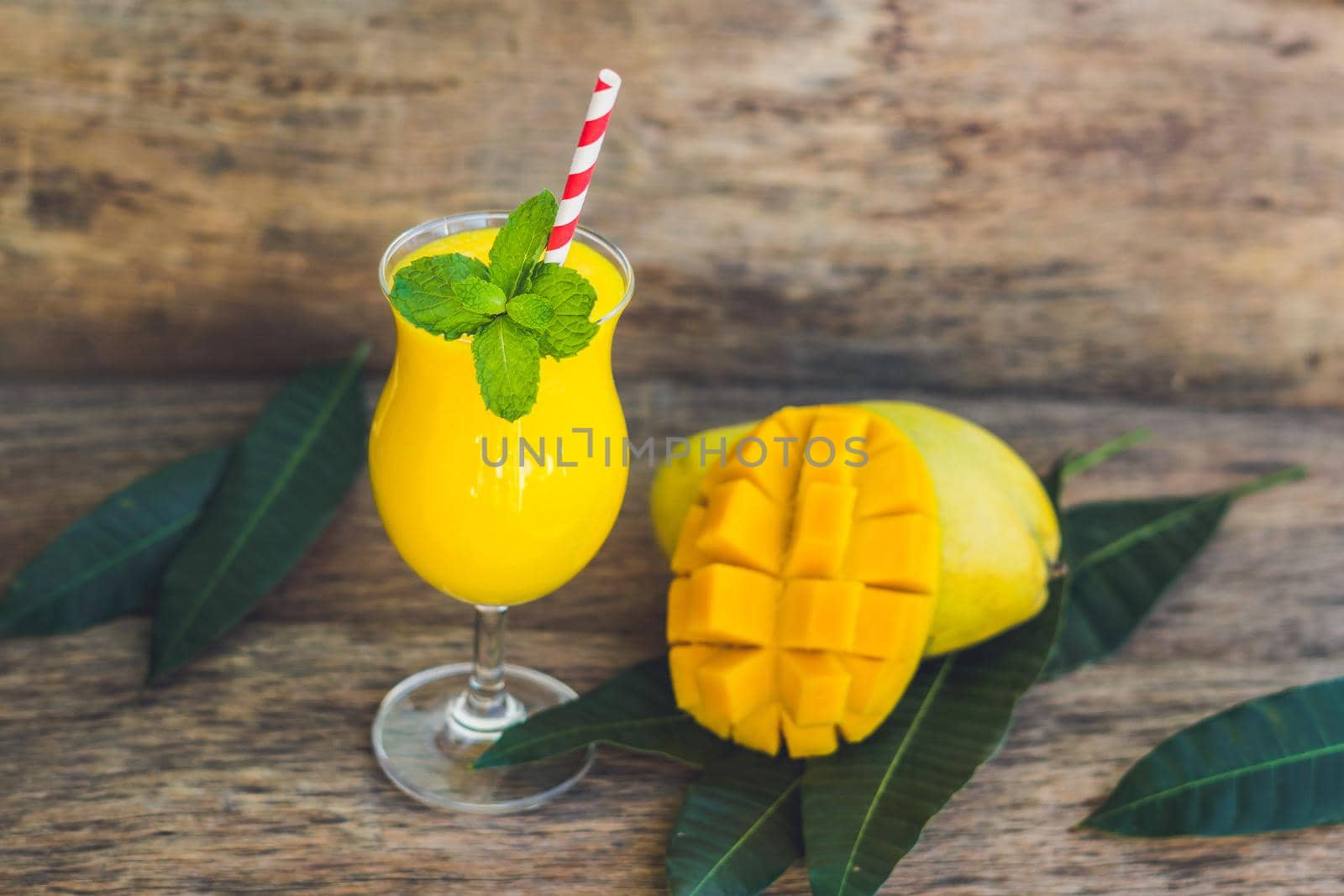 Juicy smoothie from mango in glass with striped red straw and with a mint leaf on old wooden background. Healthy life concept, copy space.