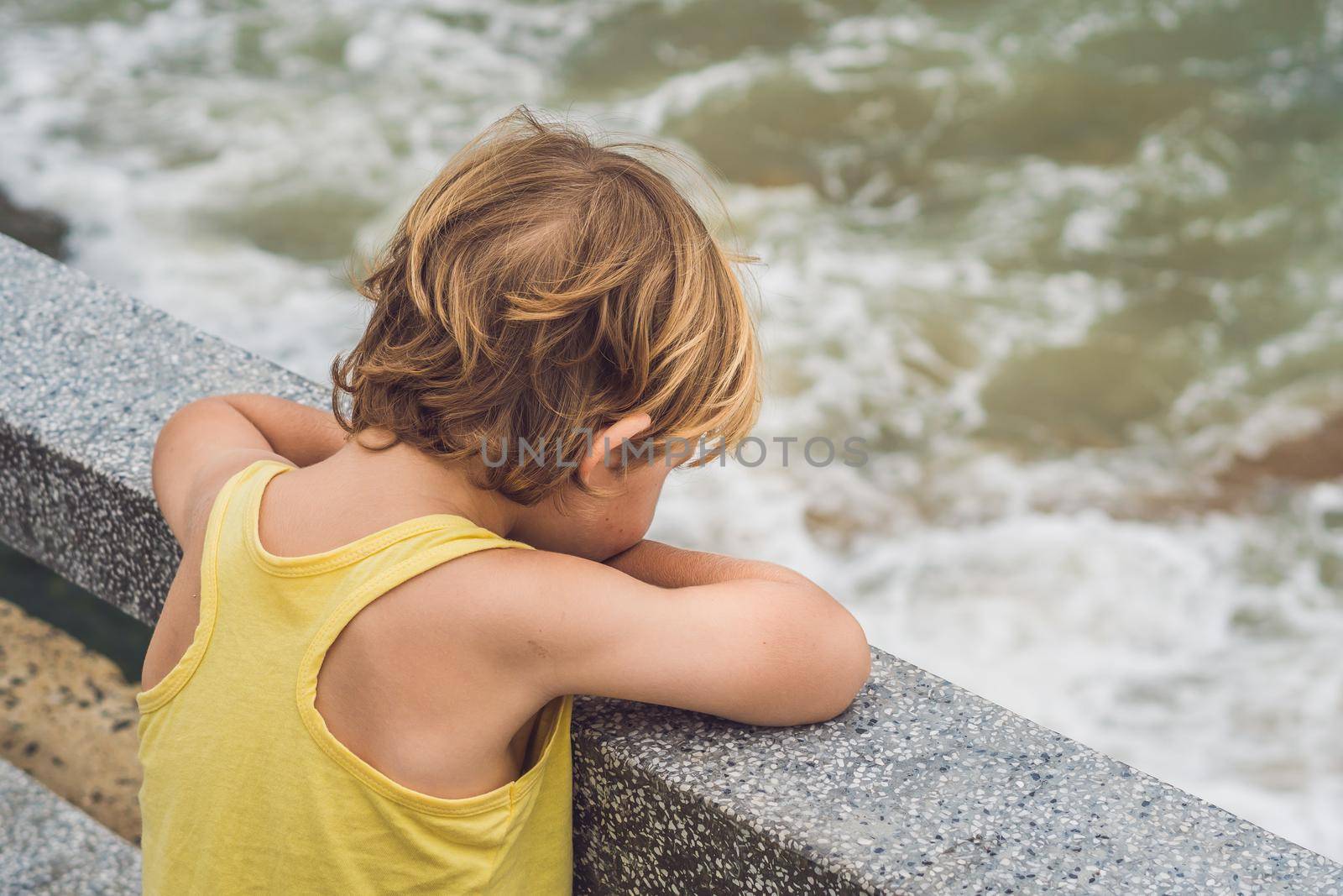 Cute boy stands on the shore watching the ocean waves.