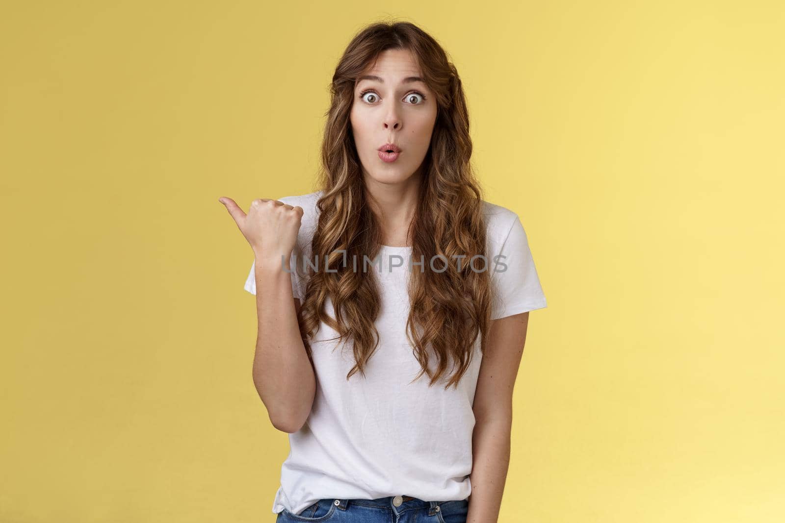 Wow interesting. Impressed surprised cute charismatic european girl curly haircut folding lips admiration fascintated pointing thumb left stare camera curious discuss gorgeous outfit coworker wear by Benzoix