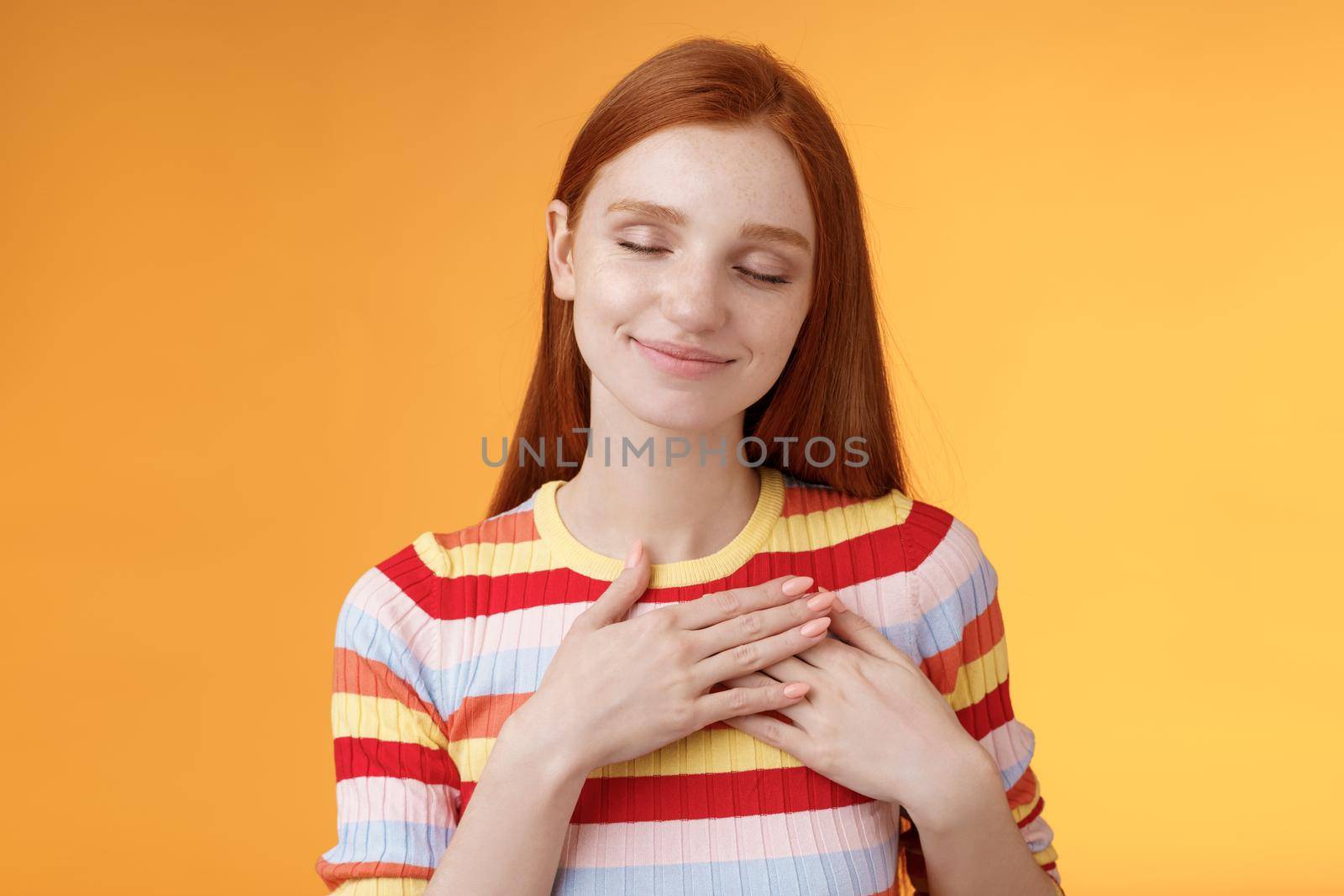 Heart keeps warm save dearest memories inside. Smiling tender heartwarming redhead lovely girl touch chest grinning closed eyes recall lovely nice moment standing romantic orange background by Benzoix