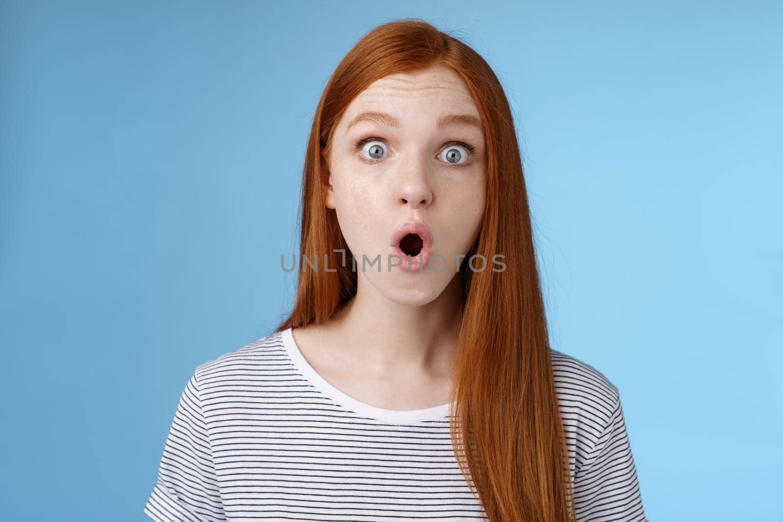 Wow omg fascinating. Impressed surprised amused good-looking redhead girl folding lips astonished wide eyes stunned reacting incredible cool promo standing blue background speechless.