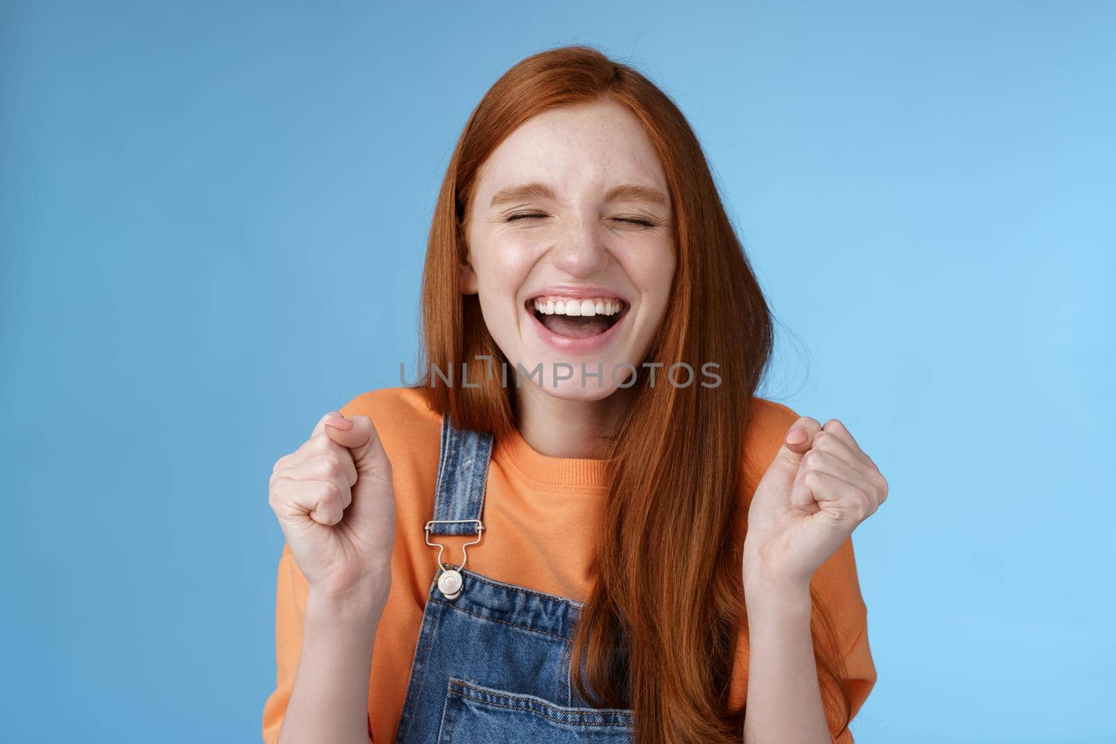 Lifestyle. Sincere happy rejocing ginger girl close eyes smiling broadly say yes waving clenched fists joyfully celebrate enterting university dream come true winning prize triumphing cheerfully blue background.