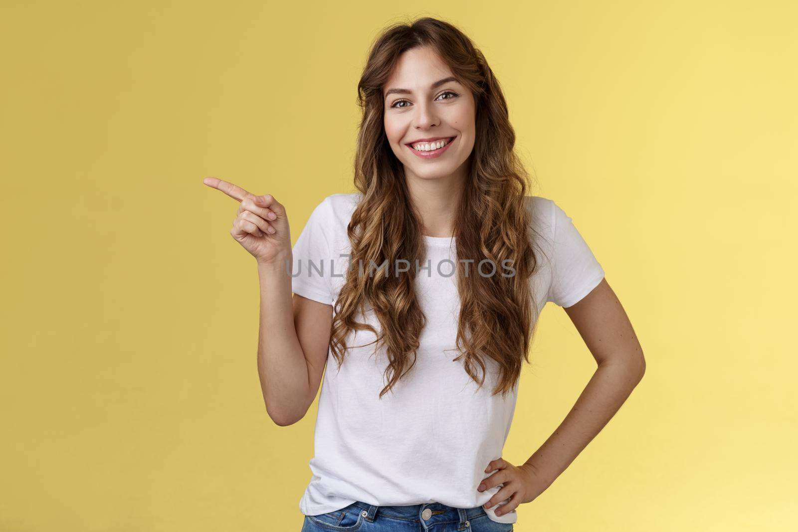 Confident sassy good-looking young friendly woman grinning satisfied tilt head lovely glad gaze hold hand waist self-assured pointing left give friend recommendation directing location good promo. Lifestyle.
