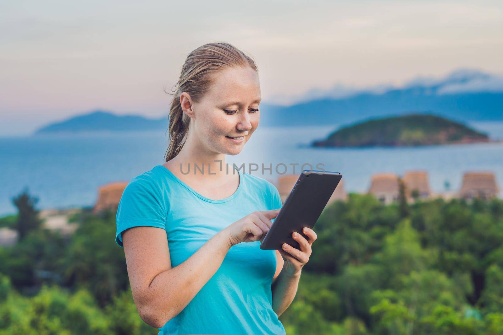 Young woman enjoys a tablet on the background of the sea.