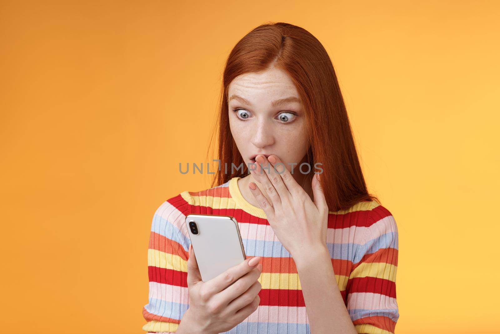 Woman receive shocking message gasping cover mouth palm staring smartphone display found out who follow boyfriend internet social network standing amazed thrilled, orange background.