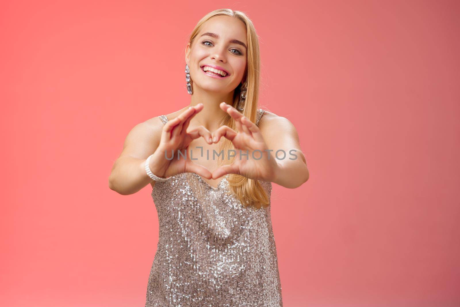 Girl confess she loves you. Portrait charming tender feminine young glamour blond woman in silver stylish glittering dress extend arms camera show heart sign smiling broadly, adore girlfriend.