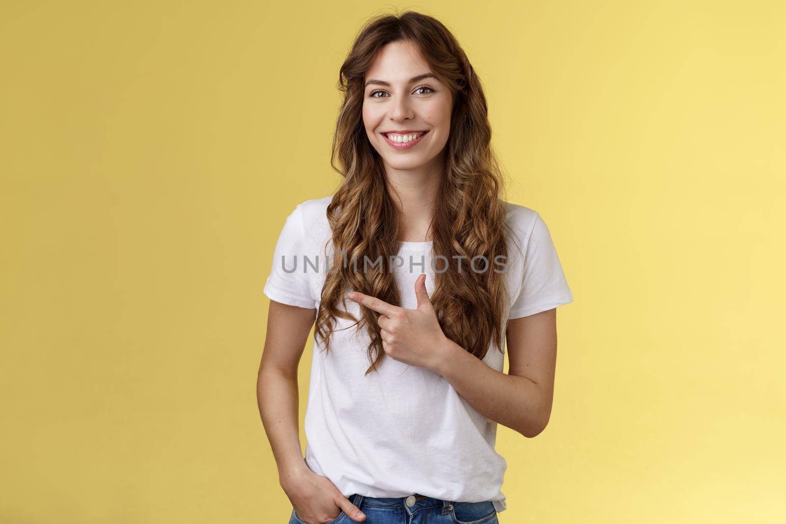Sassy confident happy charismatic young woman long curly hairstyle hold hand pocket relaxed outgoing expression pointing left index finger inviting local cafe discuss friend favorite places by Benzoix