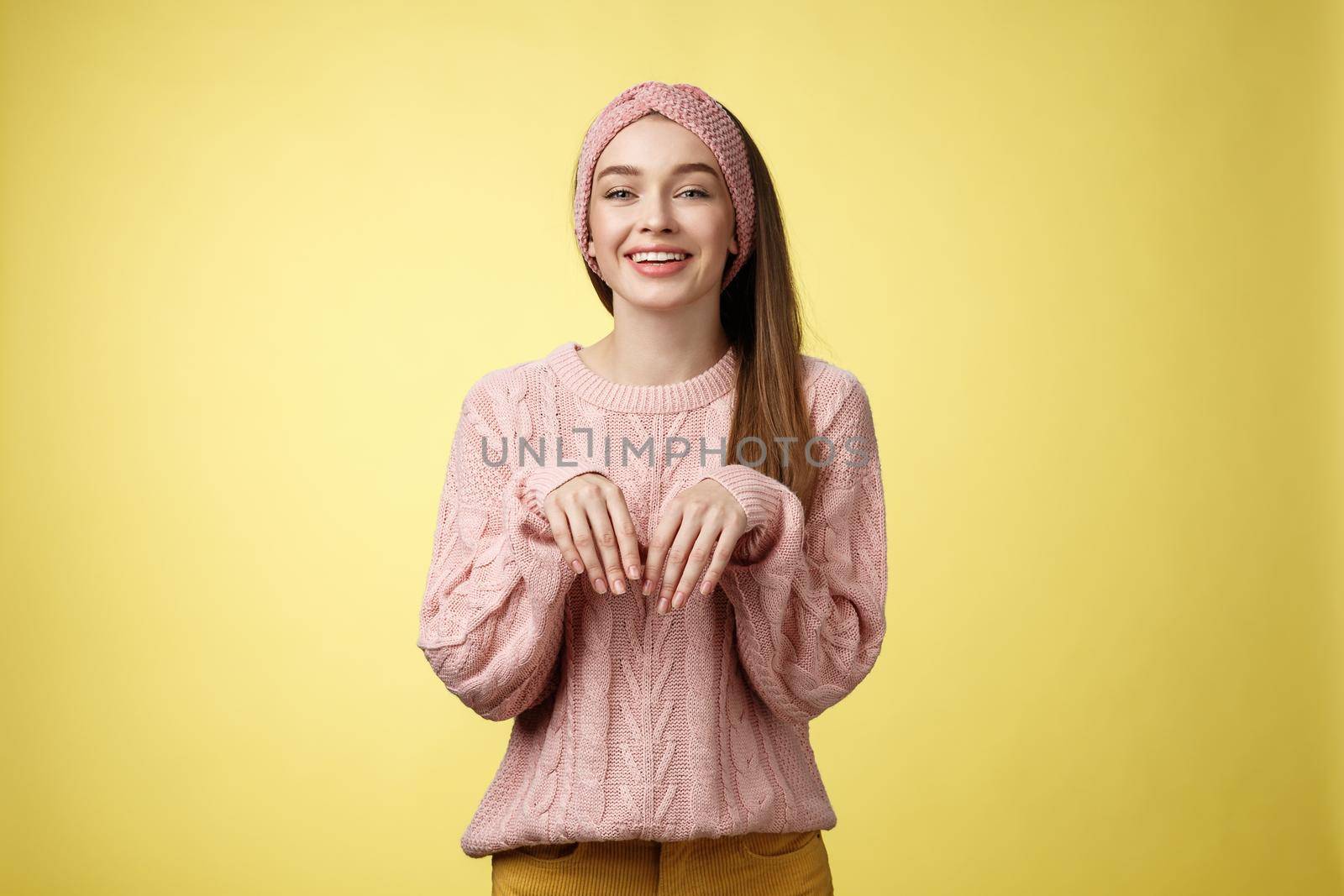 Girl pretends easter bunny. Charming cute female in knitted sweater holding palms like rabbit smiling happily, mimicking pretty animal fooling around from happiness and joy against yellow background.