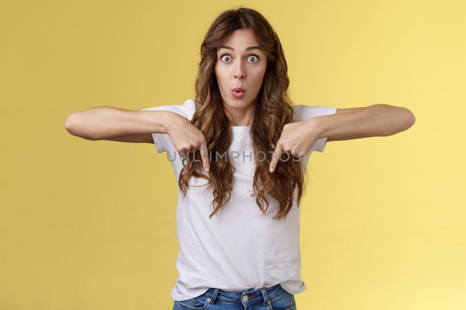 You see that too. Surprised wondered amazed happy astonished funny cheerful girl long curly haircut stare impressed amazed pointing down react fascinated curious bottom promo yellow background by Benzoix