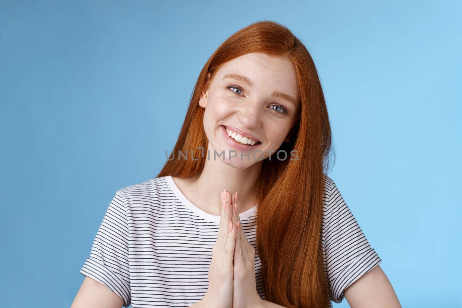Cheerful sincere kind redhead girl do coquettish eyes tilting head look nice asking favour say please smiling tender press palms together supplicating pleading begging help, standing blue background.